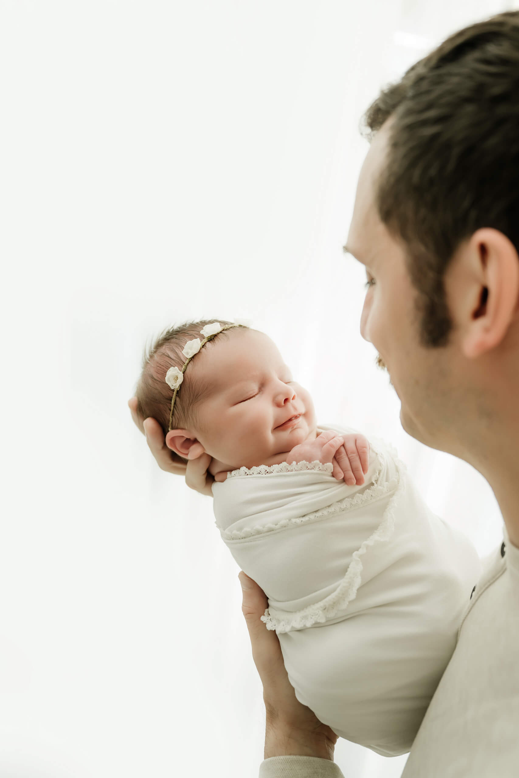 Father holding his wrapped newborn near a bright studio window, captured during a calm mini studio newborn session in Seattle.