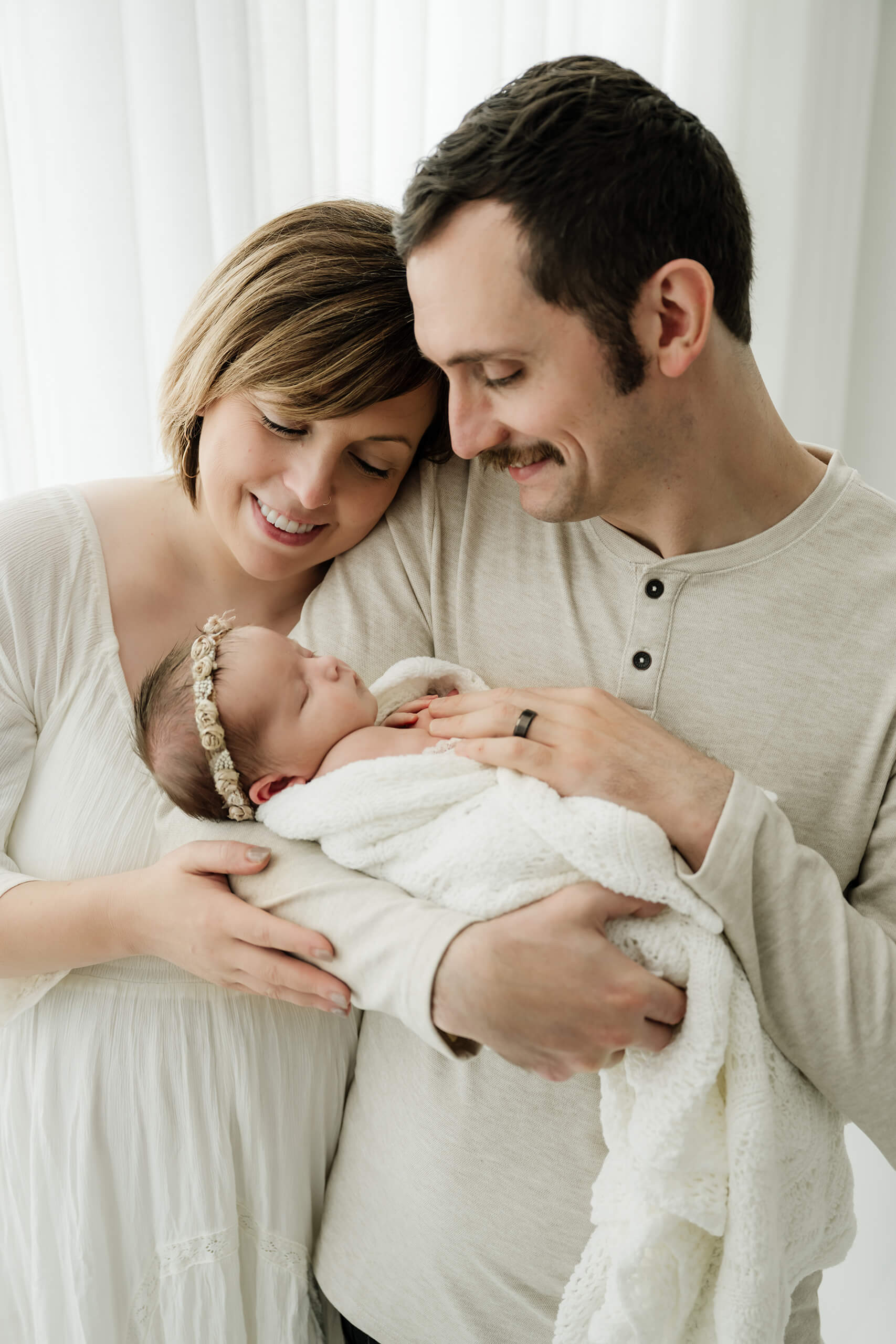 Parents standing together holding their newborn wrapped in white, captured in a light-filled Seattle studio newborn session.