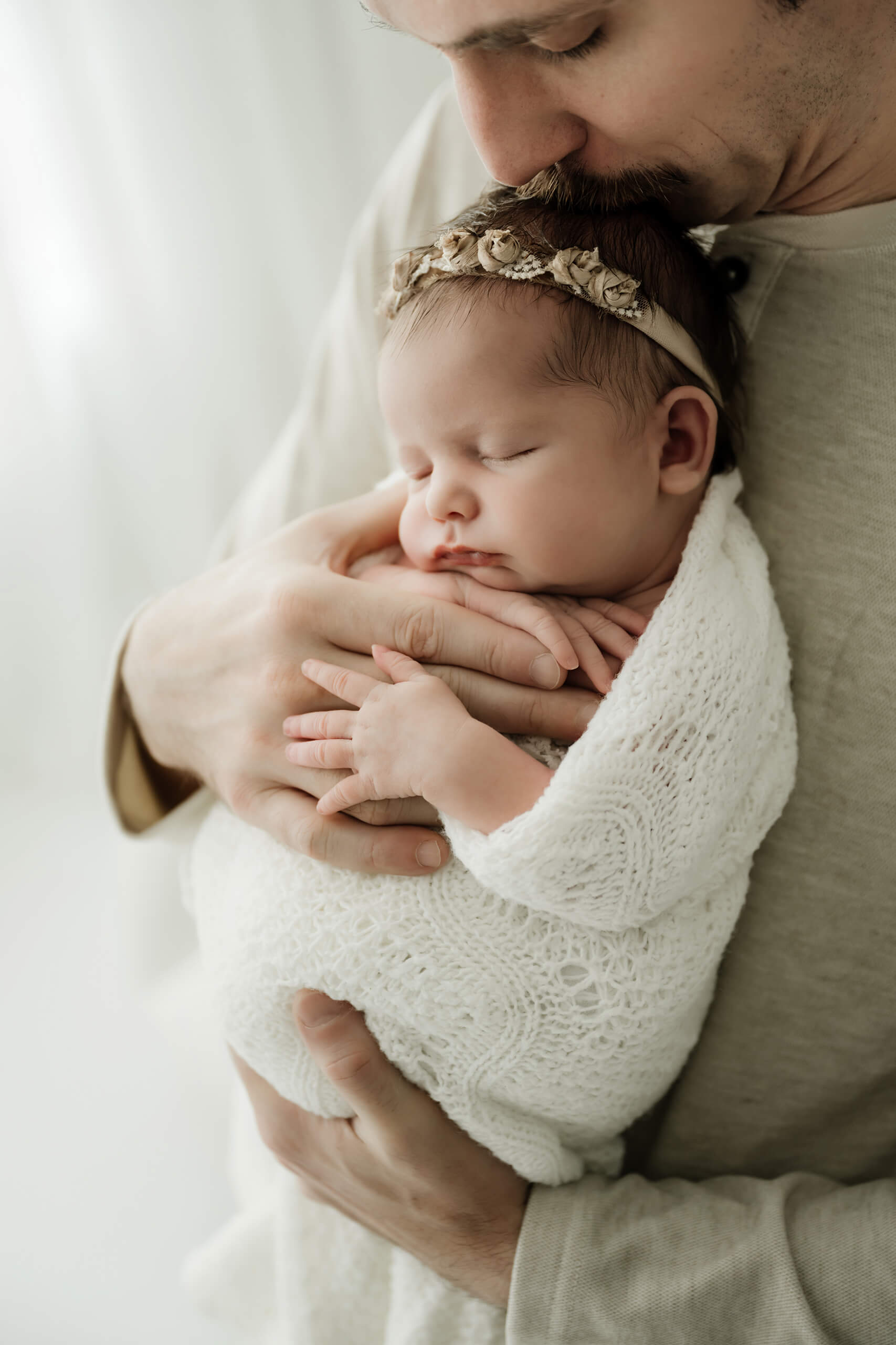 Father holding his sleeping newborn close to his chest during a simple wrapped newborn session in a Seattle studio.