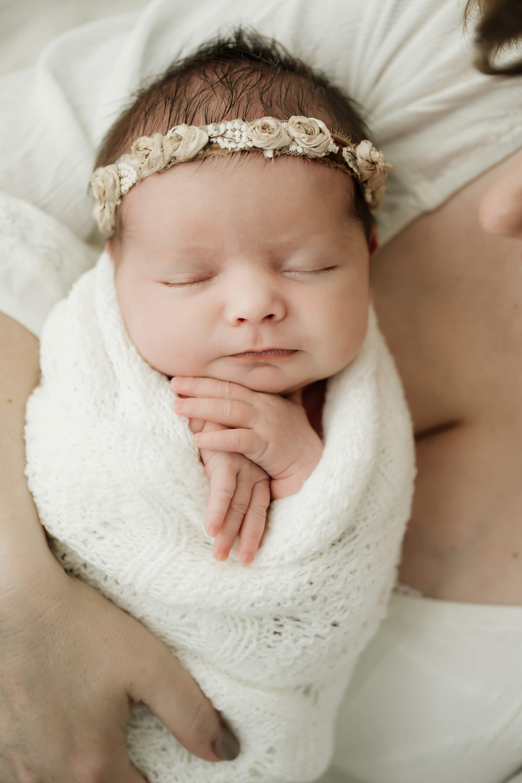 Close-up of a newborn wrapped in white with hands folded under the chin, photographed during a mini newborn session in Seattle.