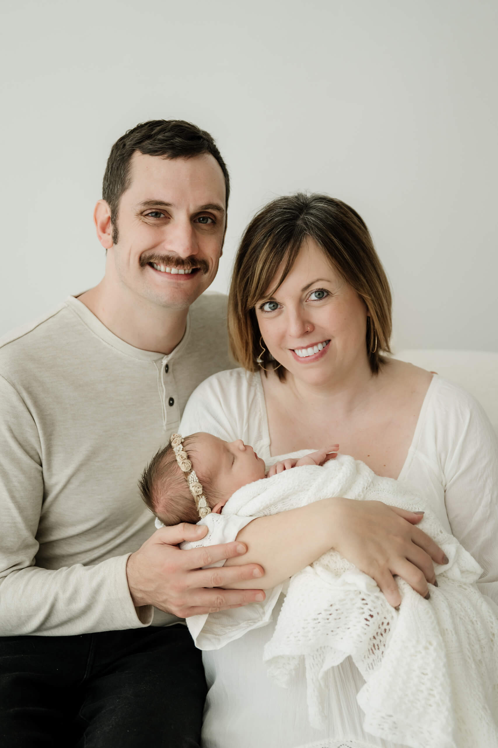 Parents smiling softly while holding their newborn, captured in a natural, baby-focused studio session in Seattle.