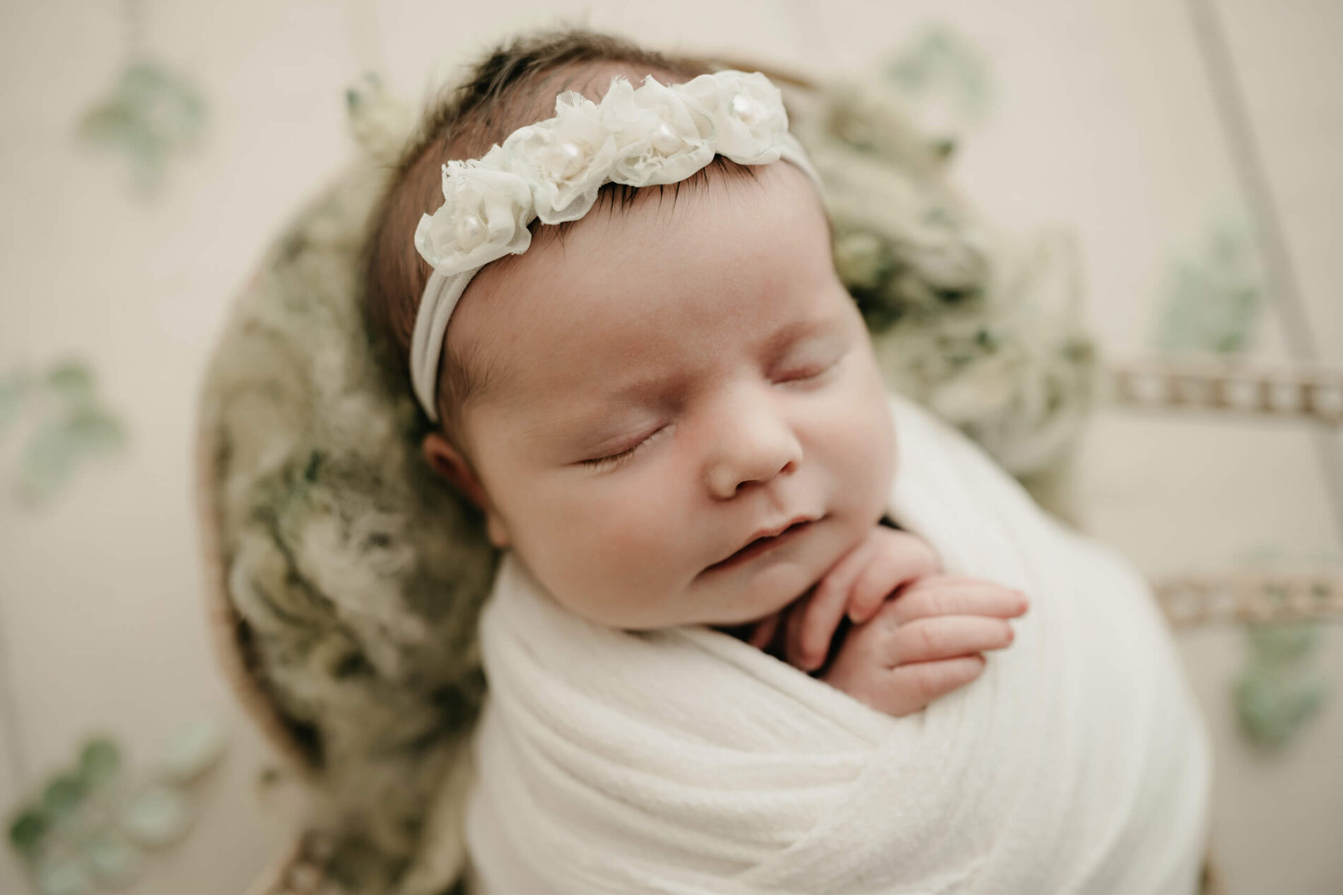 Newborn baby wrapped in white with floral headband, photographed from above in Seattle newborn studio.