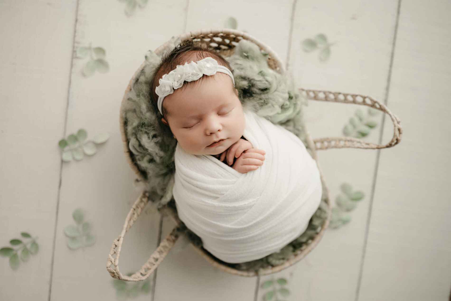 Overhead view of a wrapped newborn baby sleeping in a basket, Seattle newborn photography with neutral styling.