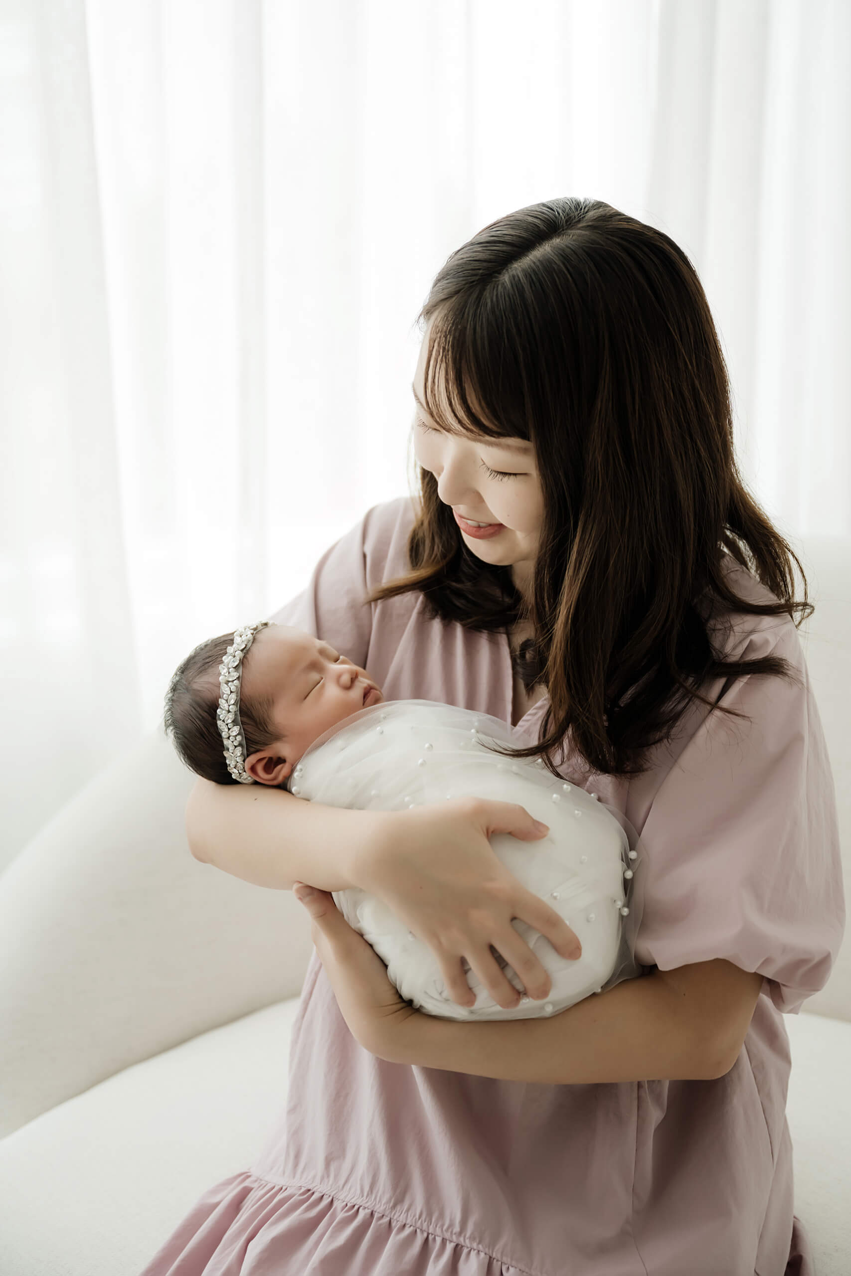 Mother holding her wrapped newborn in a soft pink dress, captured during a calm studio newborn session in Seattle.