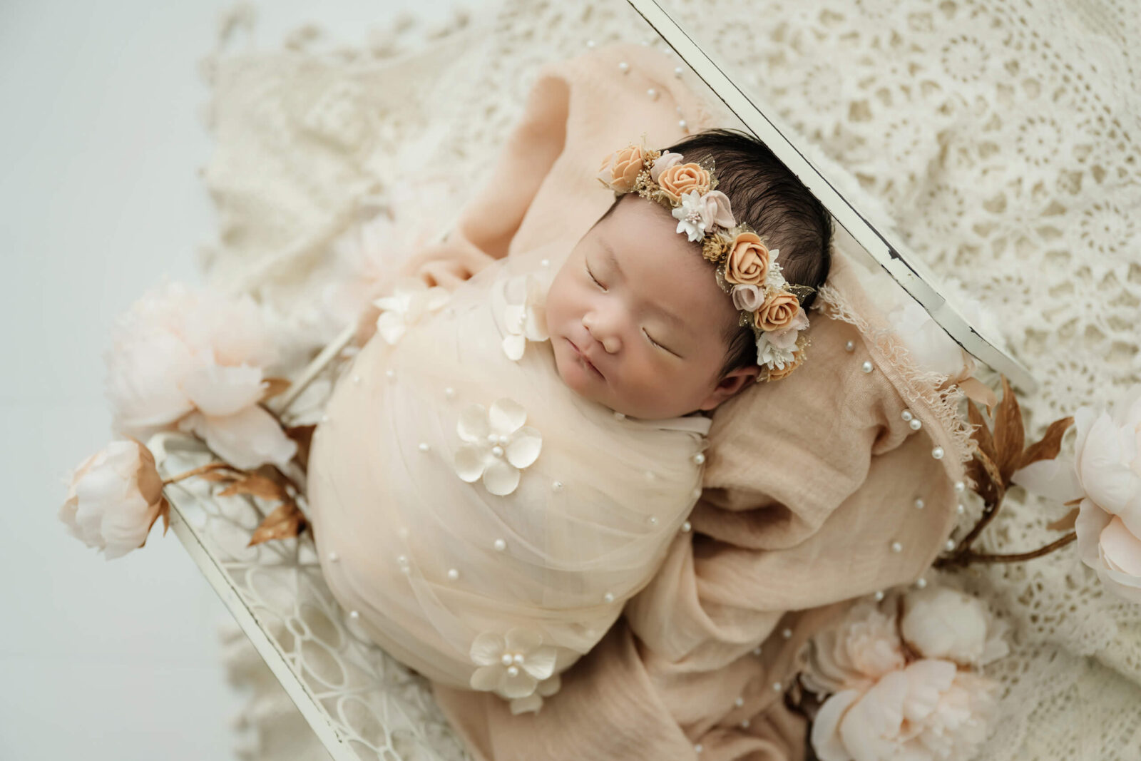 Newborn baby wrapped in neutral fabric with floral headband, posed in a basket for a simple, baby-focused Seattle studio newborn photo.