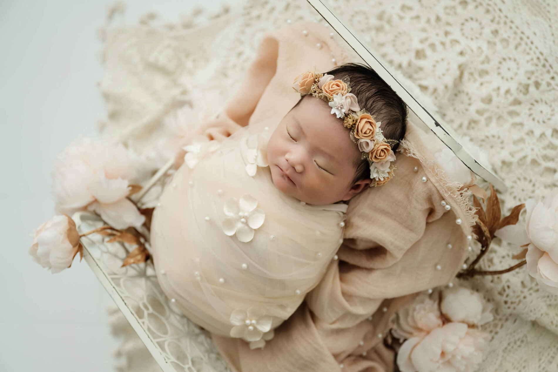 Newborn baby wrapped in neutral fabric with floral headband, posed in a basket for a simple, baby-focused Seattle studio newborn photo.