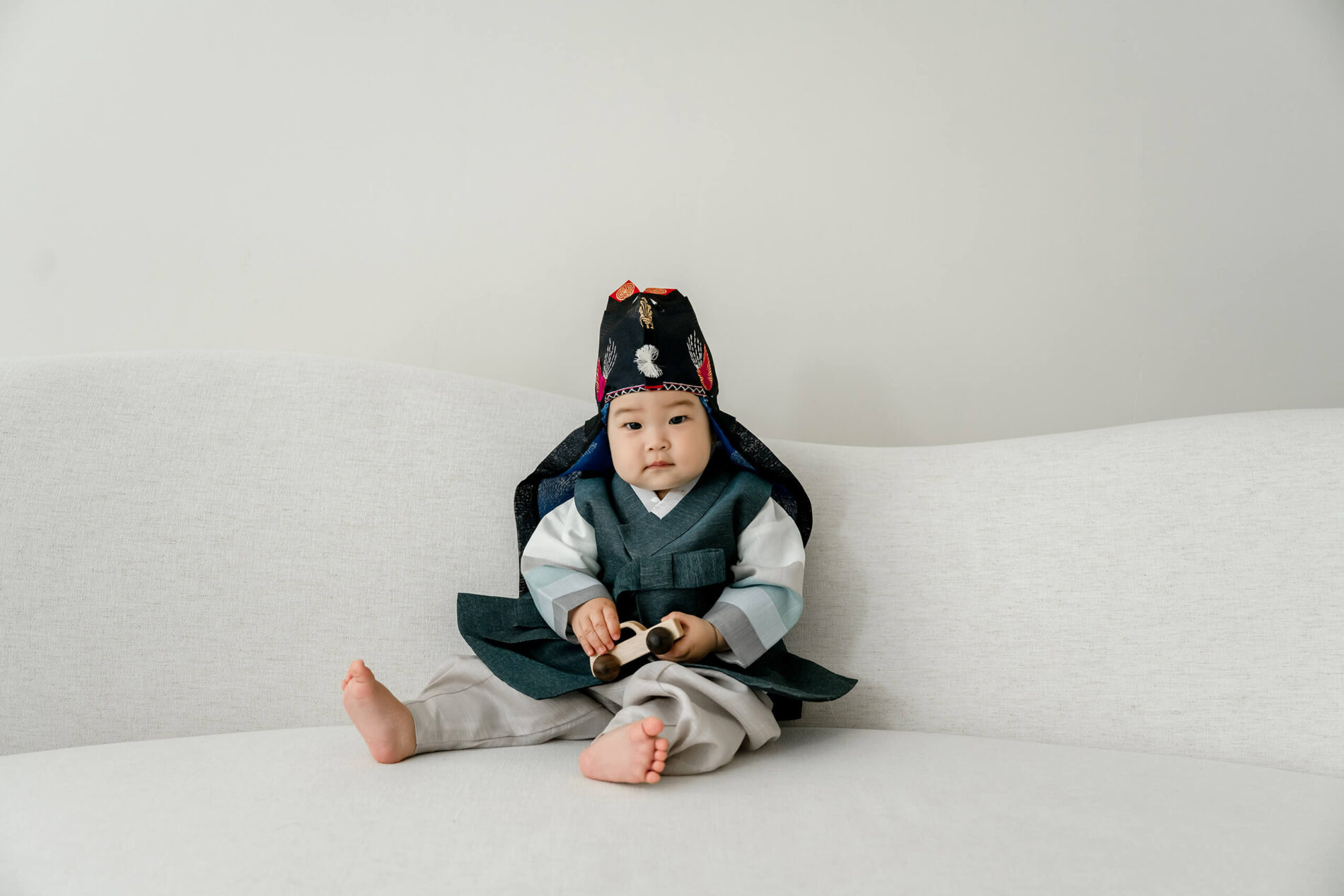 A baby wearing traditional Korean hanbok seated on a studio couch during a family session near Bellevue.