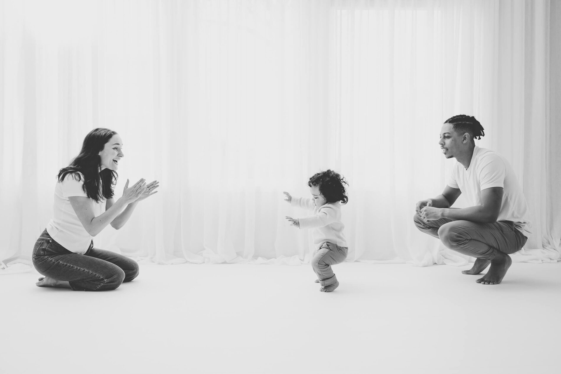 A toddler taking first steps toward parents during a family studio session in Seattle.