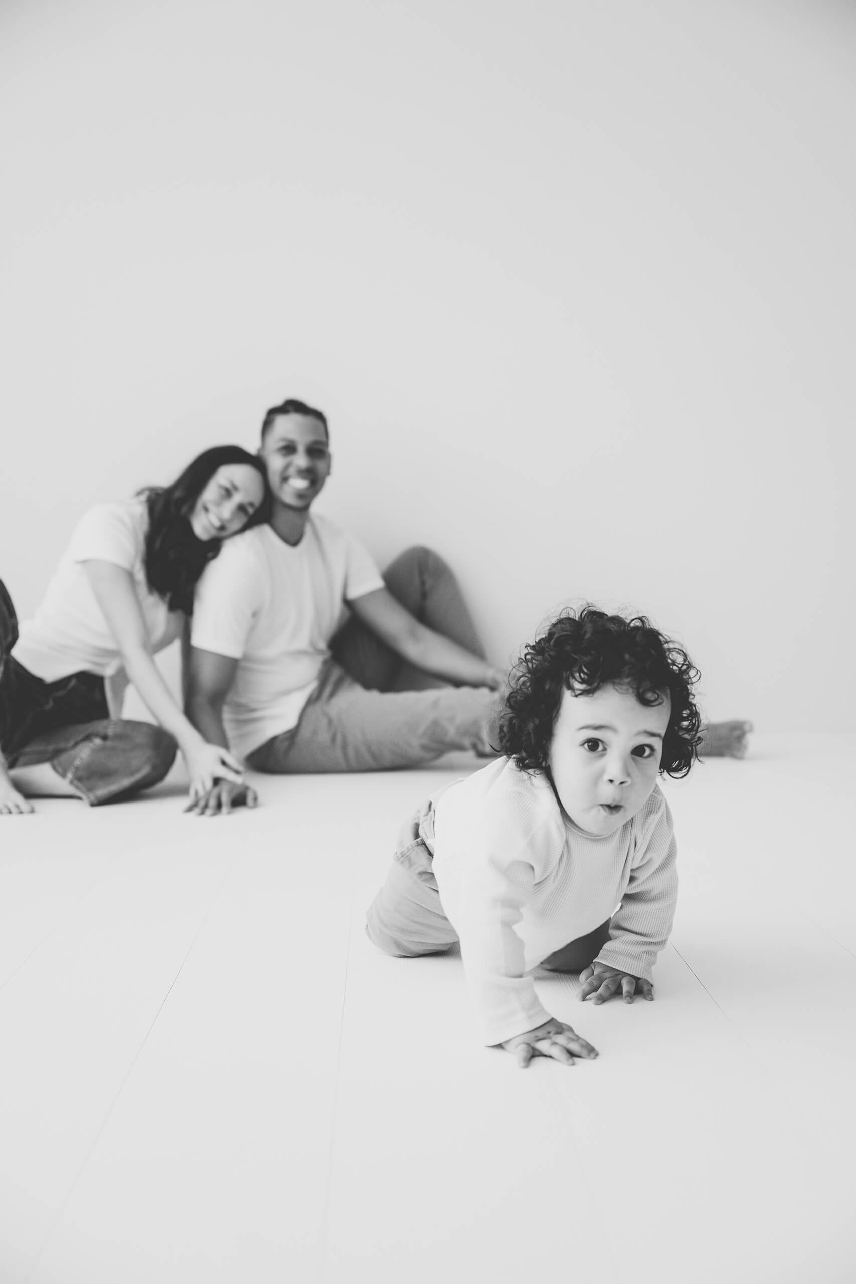A toddler crawling toward the camera while parents sit behind during a Kirkland family studio session.