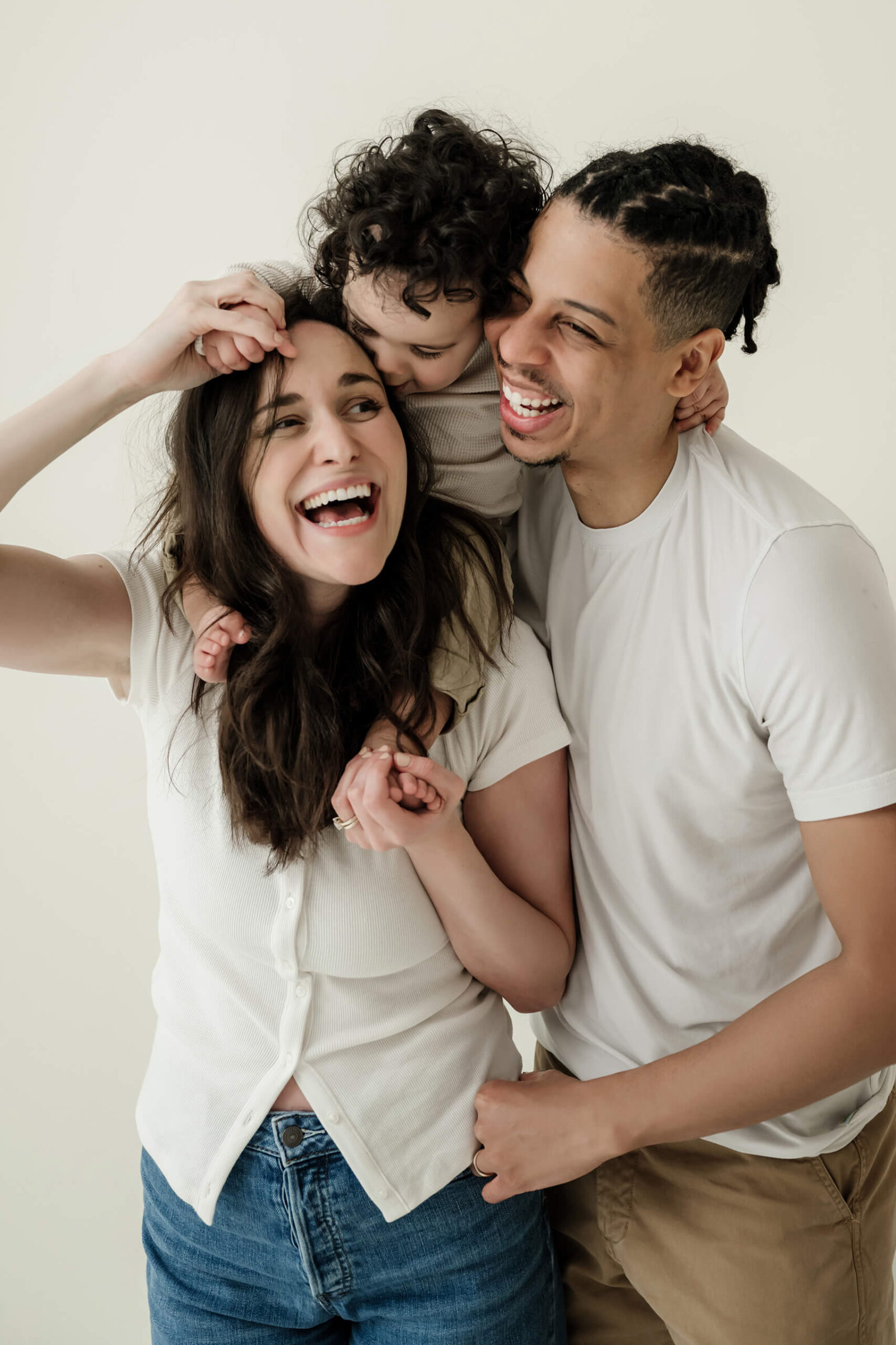 Parents laughing together while their toddler cuddles between them in a Kirkland family studio.