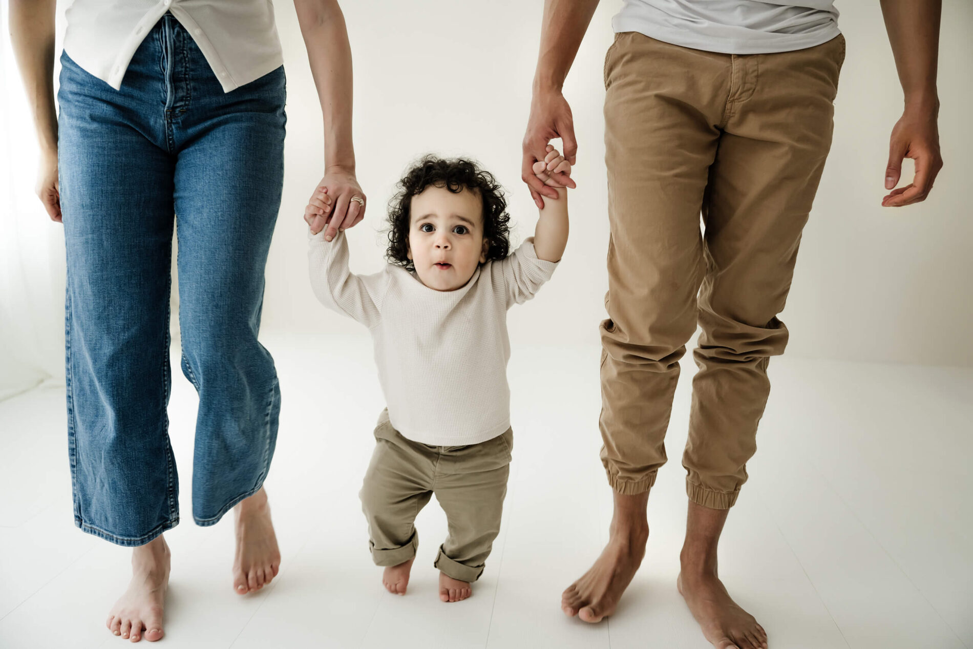 A toddler taking supported steps while holding both parents’ hands during a Seattle family studio session.