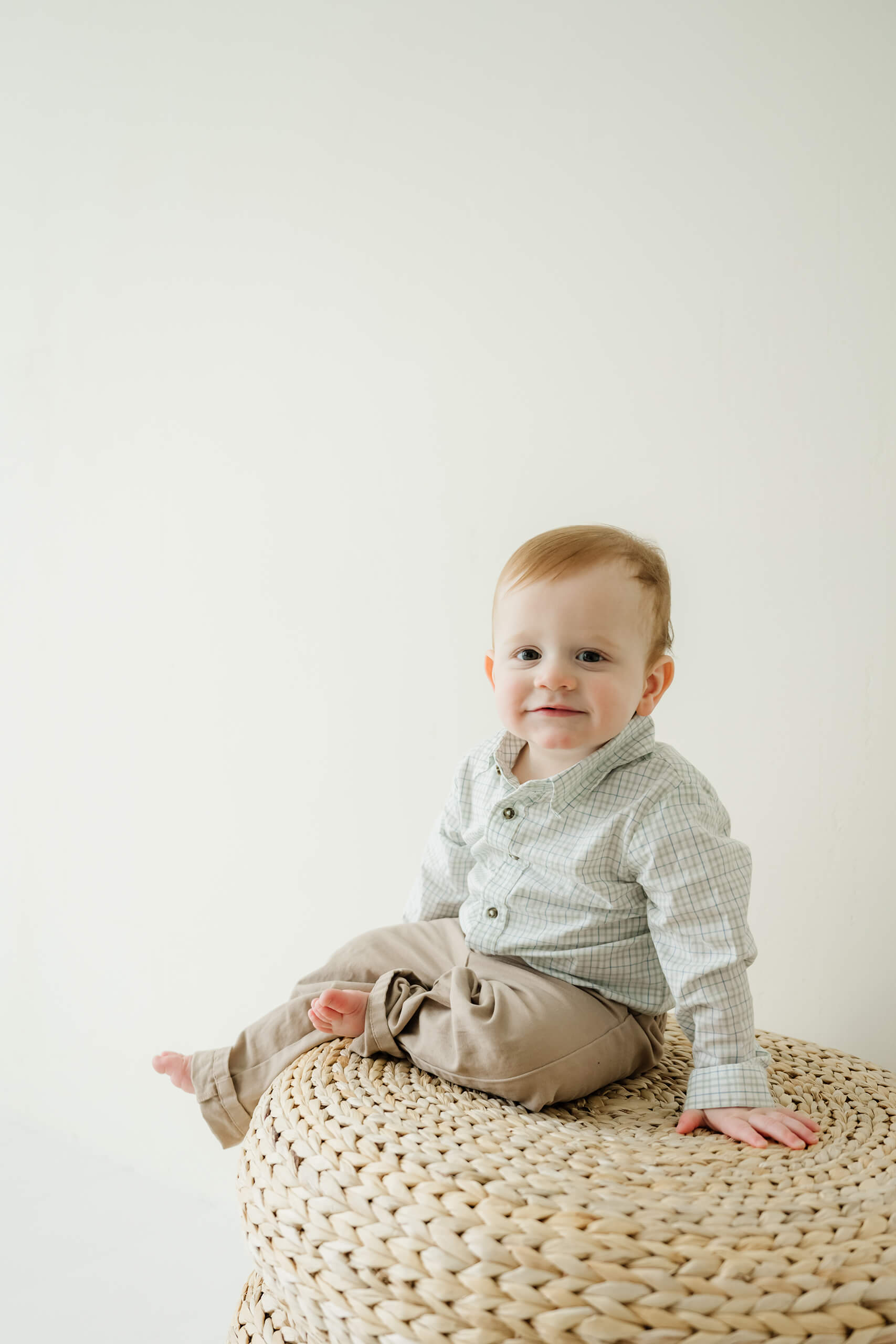 A baby boy sitting on a woven stool during a Seattle family studio photography session.