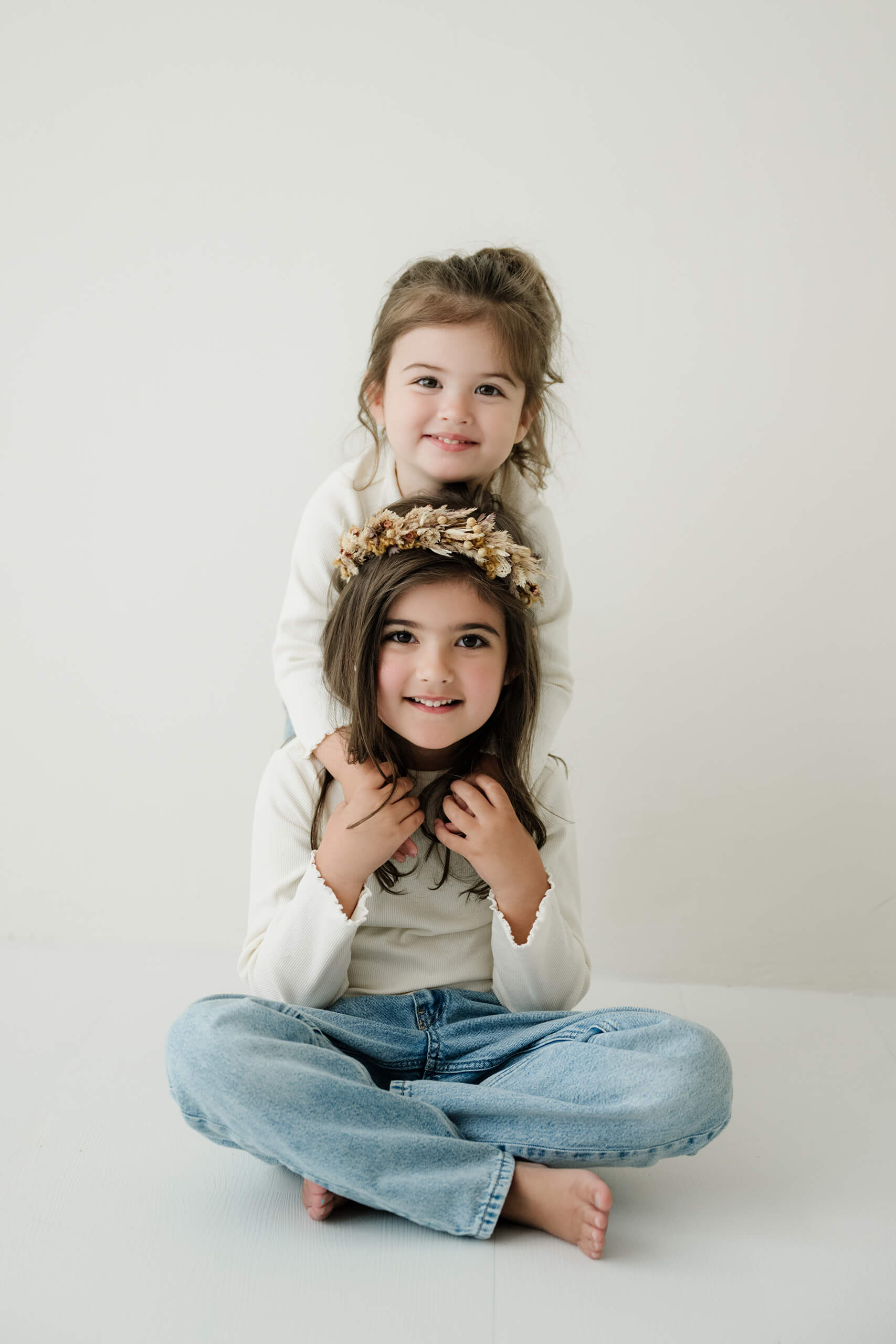 Two sisters sit together in a minimalist studio setting during a Seattle family photography session.