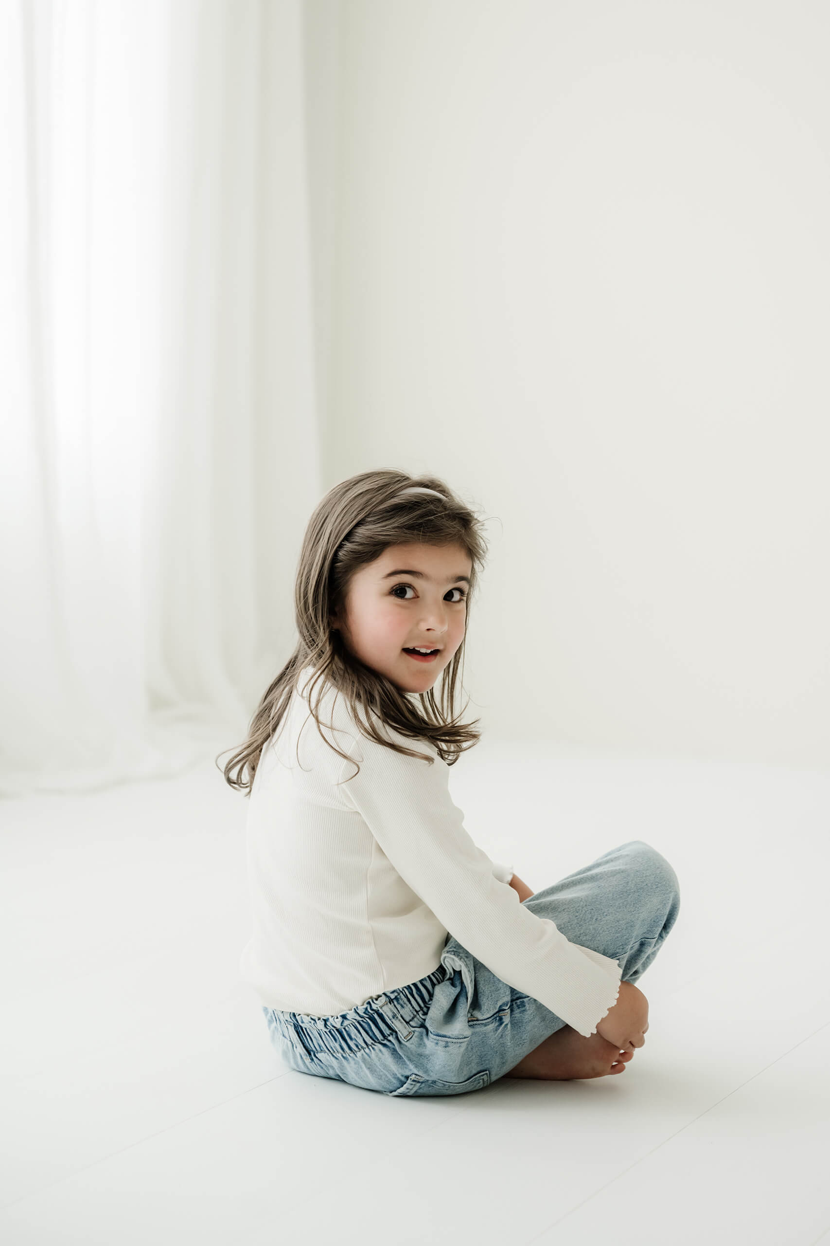 A young girl sits barefoot on the studio floor during a timeless family session in Kirkland.