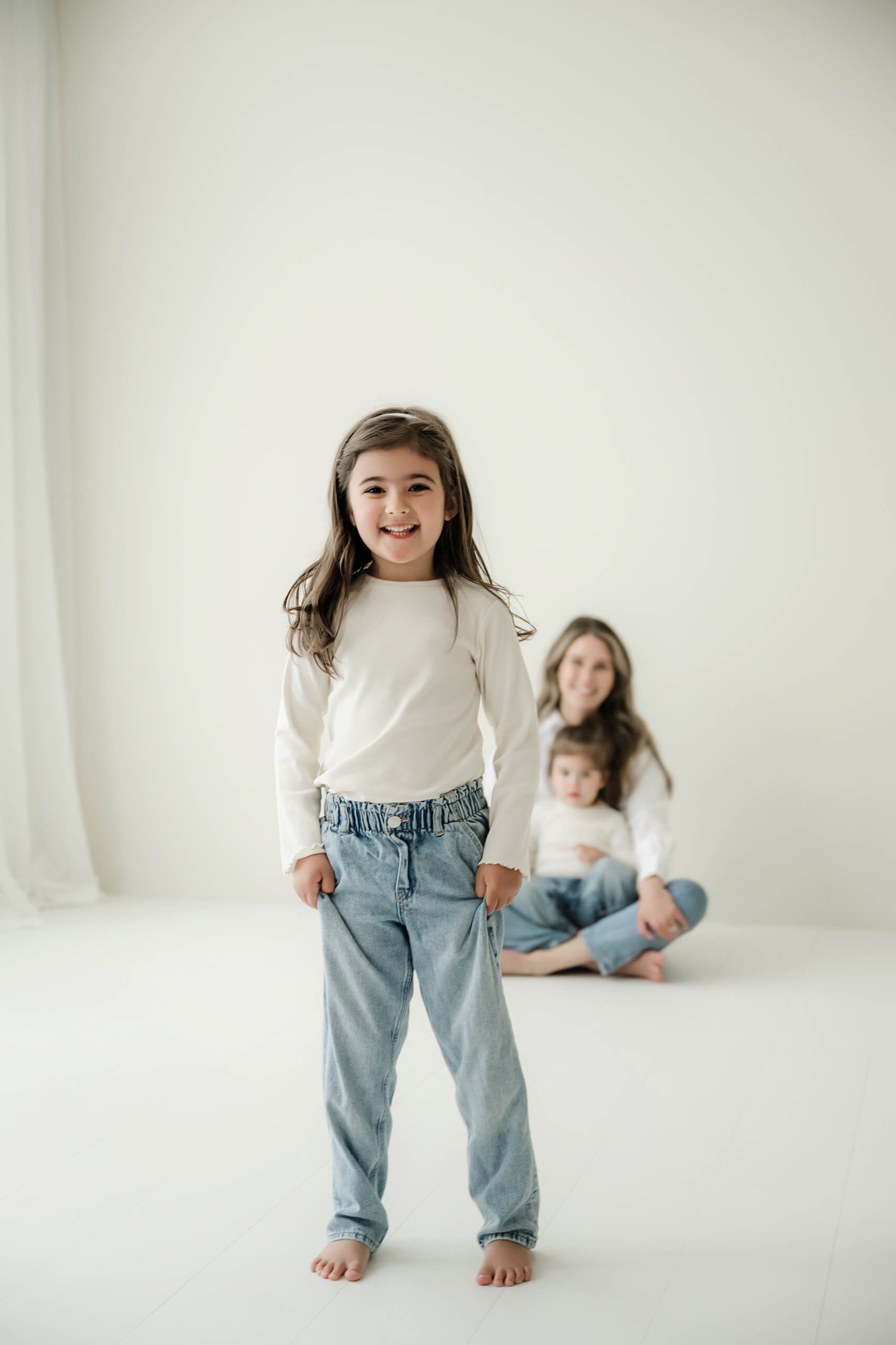 A child stands confidently in the foreground while her family sits behind her in a Seattle studio family session.