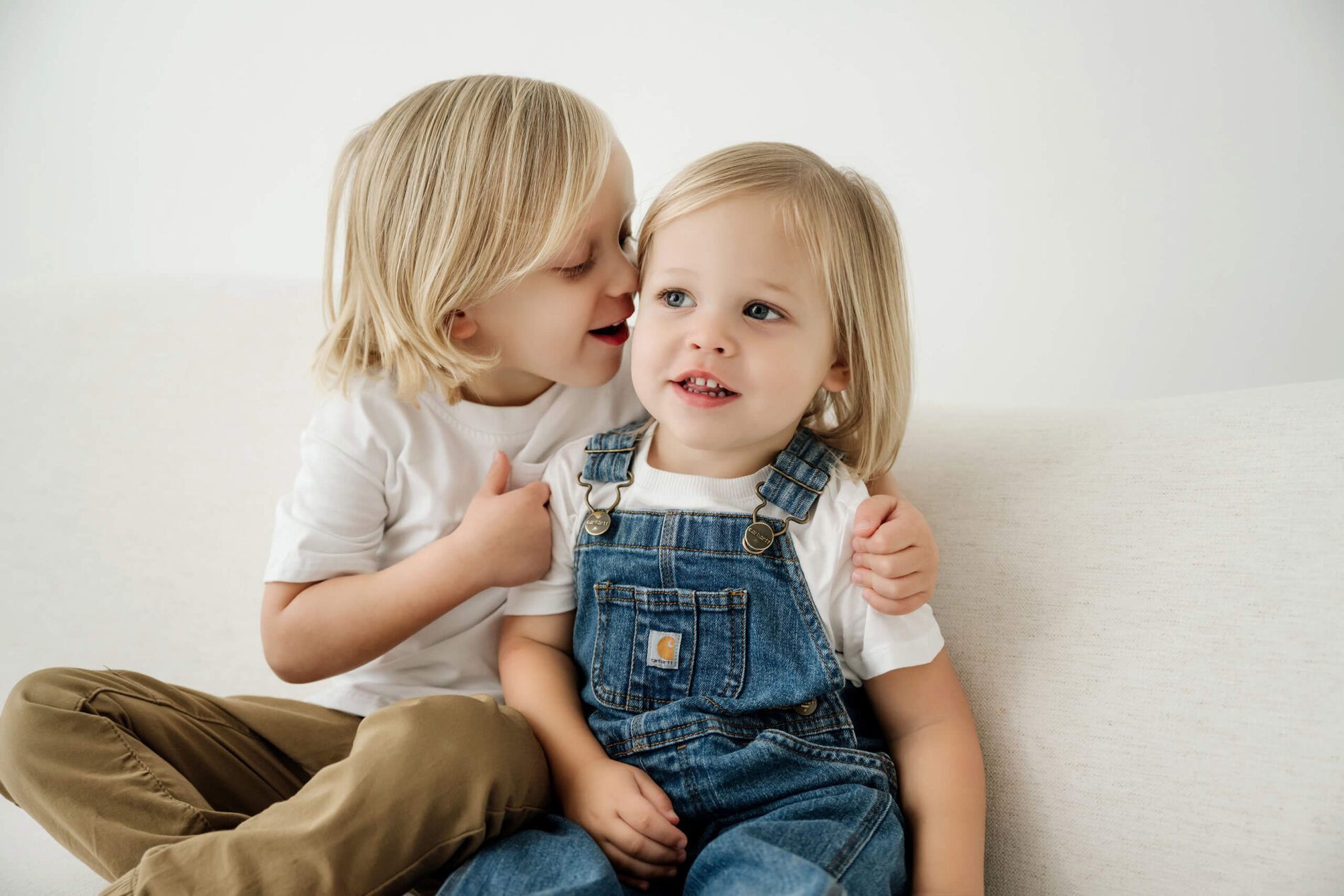 An older sibling leans in to whisper to a younger sibling during a Bellevue studio family session.