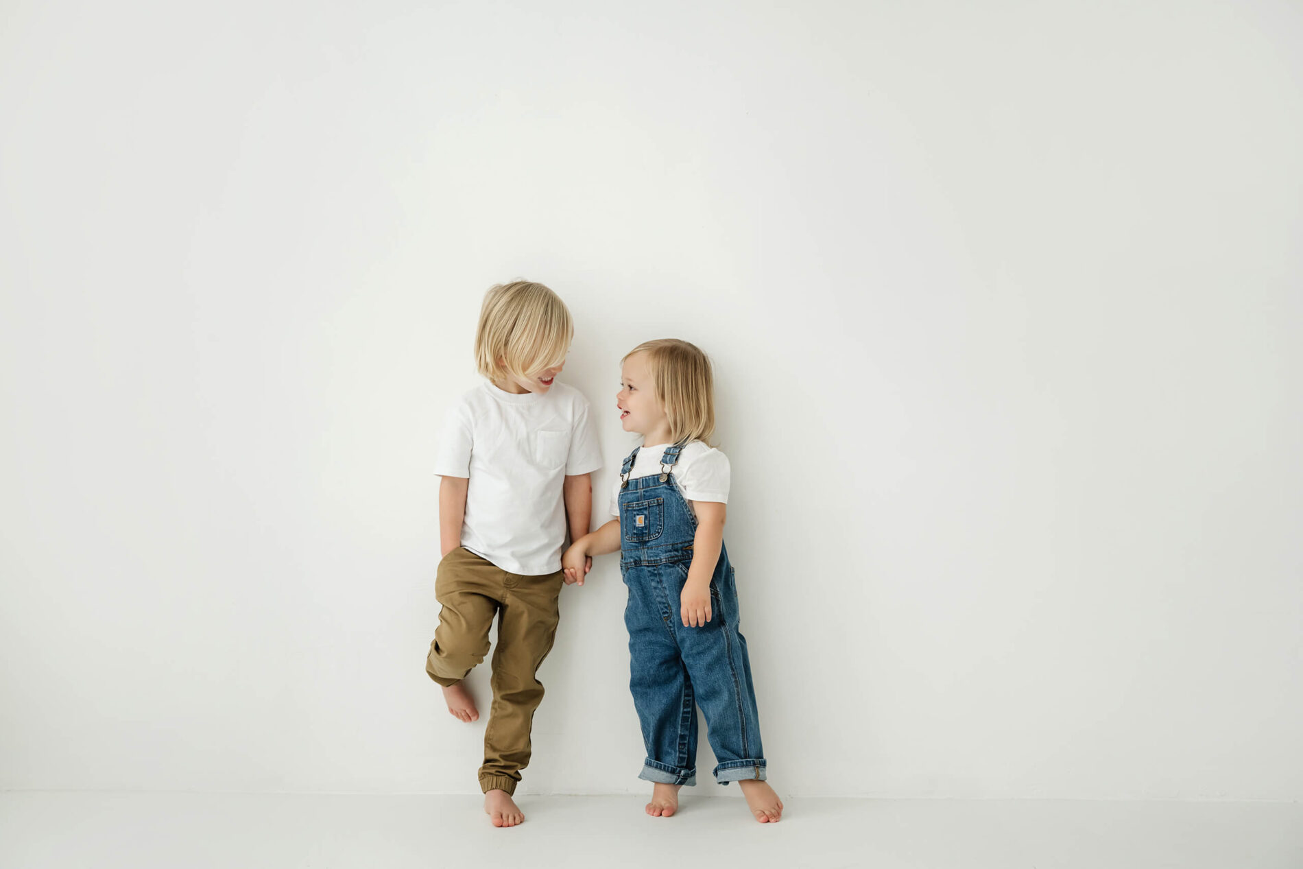 Two siblings stand side by side against a white backdrop during a Seattle studio family session.