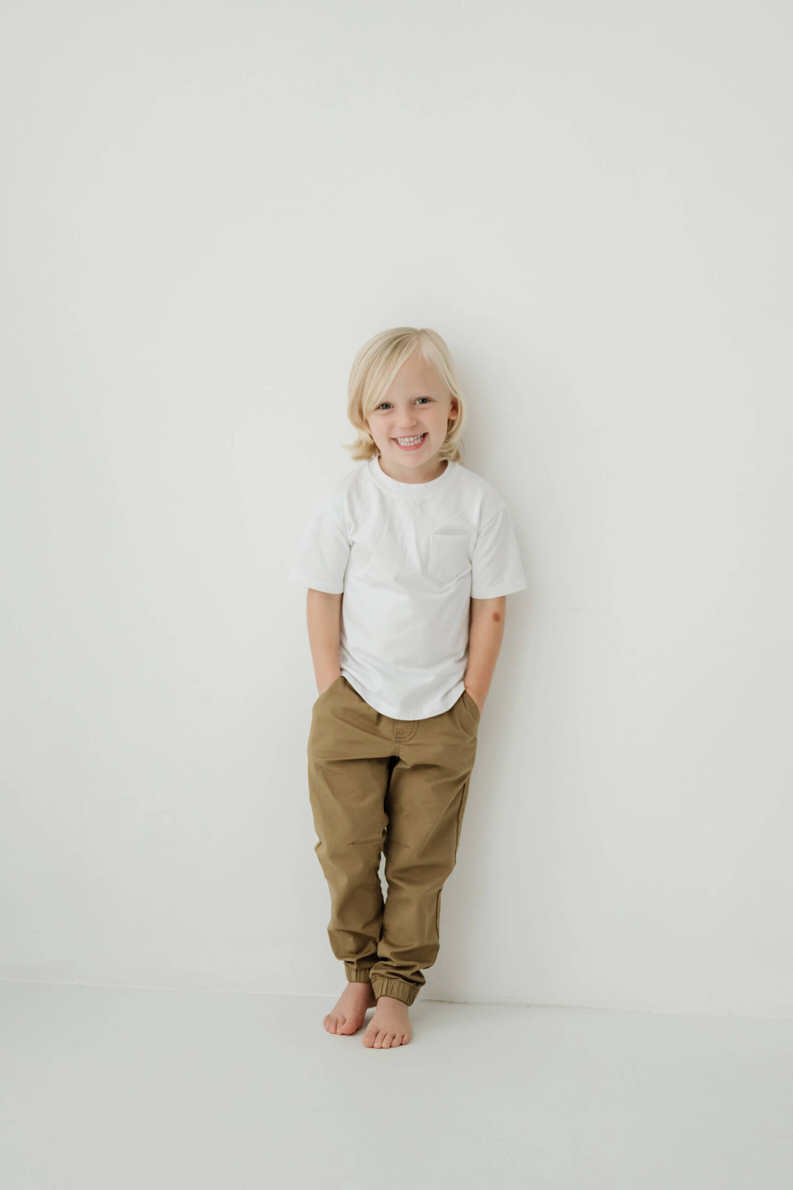 A child stands barefoot against a white wall during a minimalist family studio session near Seattle.