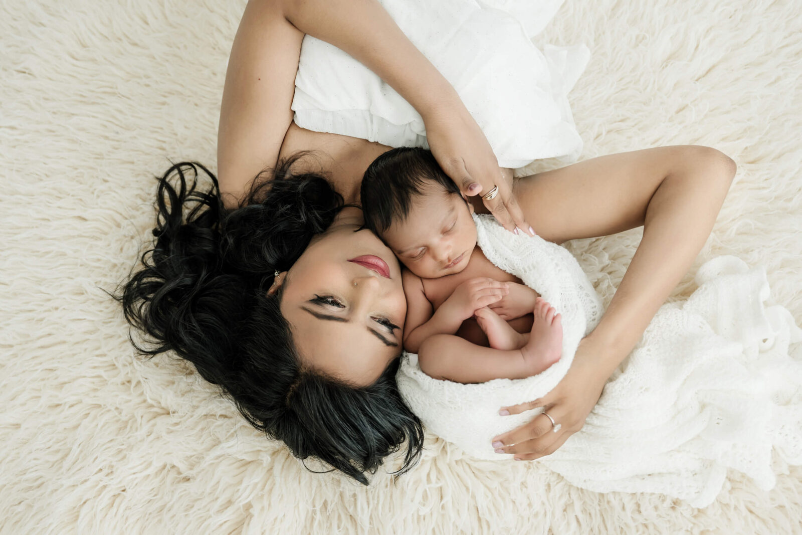 Mother lying with her 16 day old newborn wrapped in a white blanket during a Seattle studio newborn photoshoot