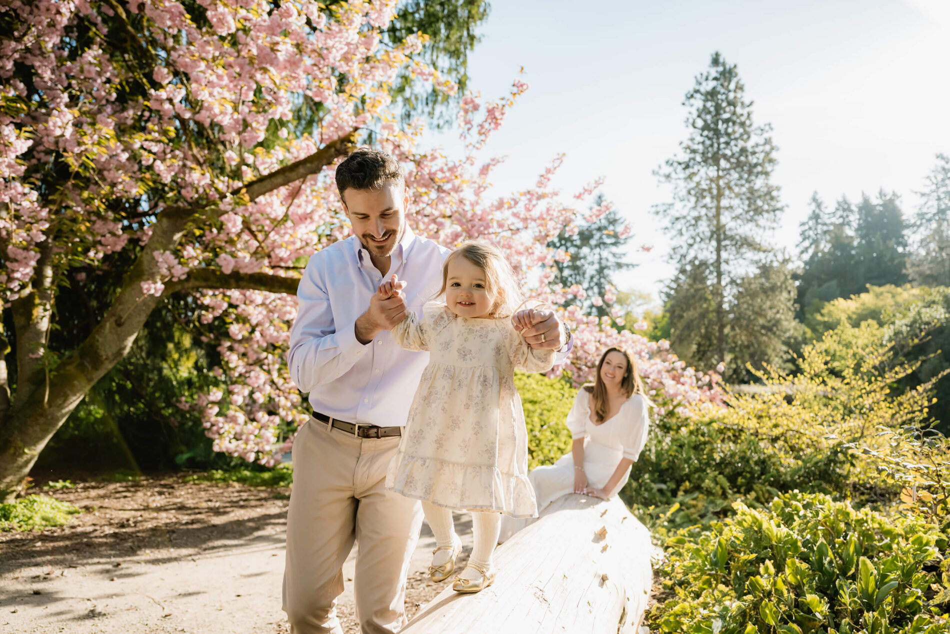 Father helping toddler daughter balance on a log during a spring family photo session at Washington Park Arboretum