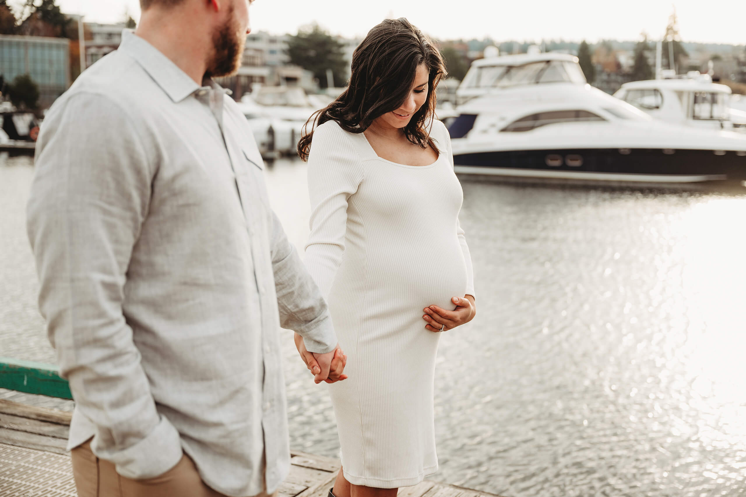 Expecting mother holding her baby bump while walking hand in hand with her partner at Kirkland Marina.
