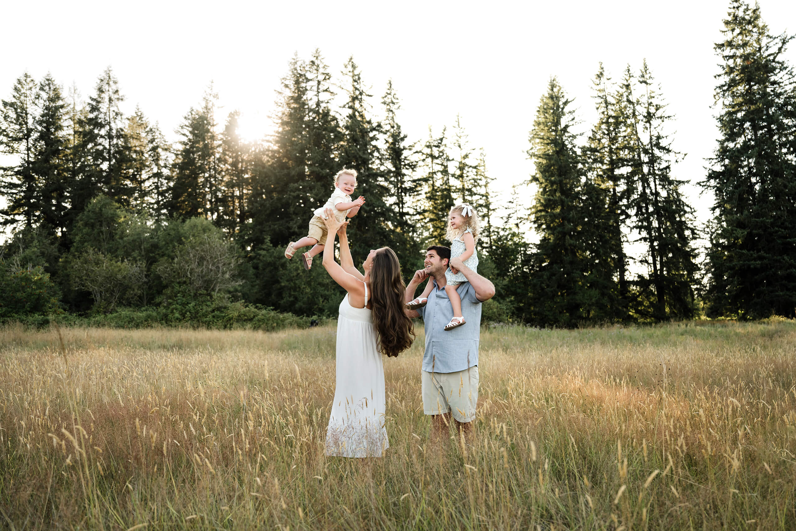 Parents playing with their two young children in a tall grass field during a summer family photo session.