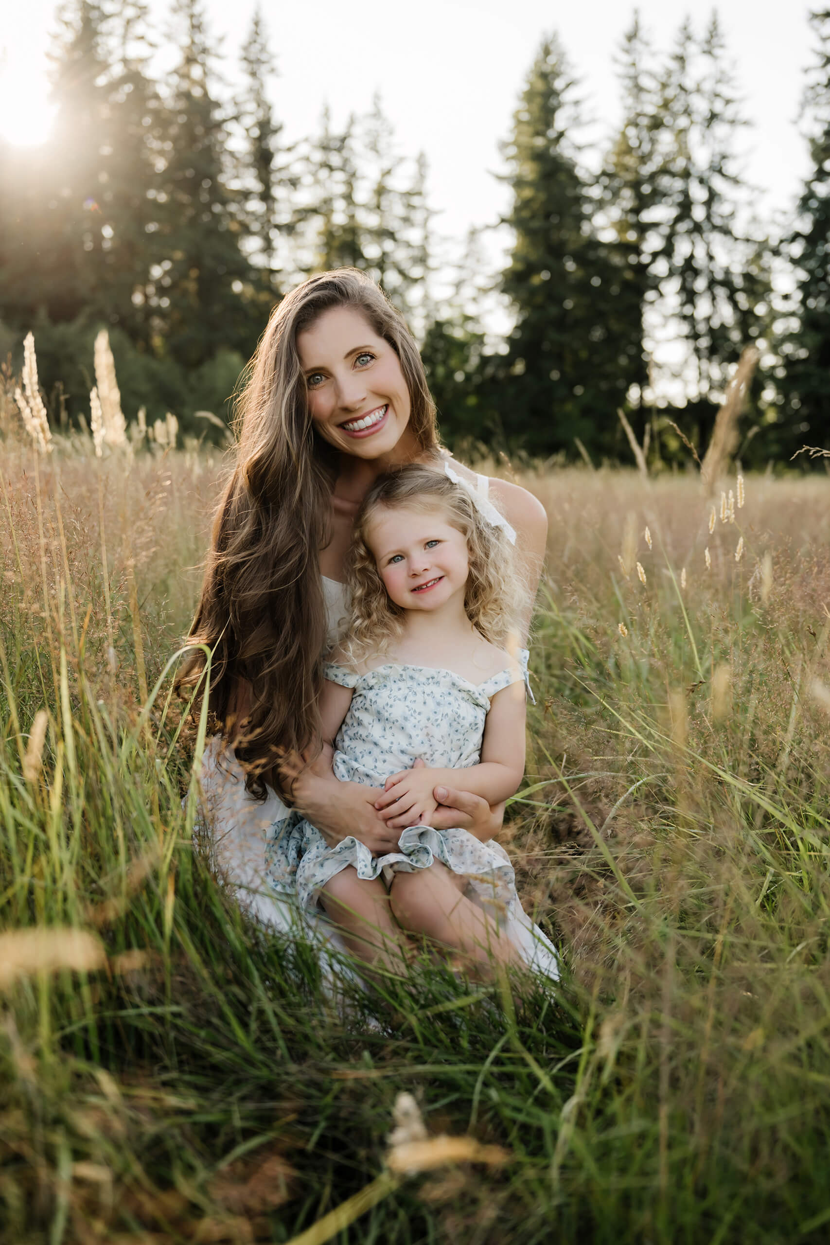 Mother and daughter sitting together in tall golden grass during an outdoor family session.