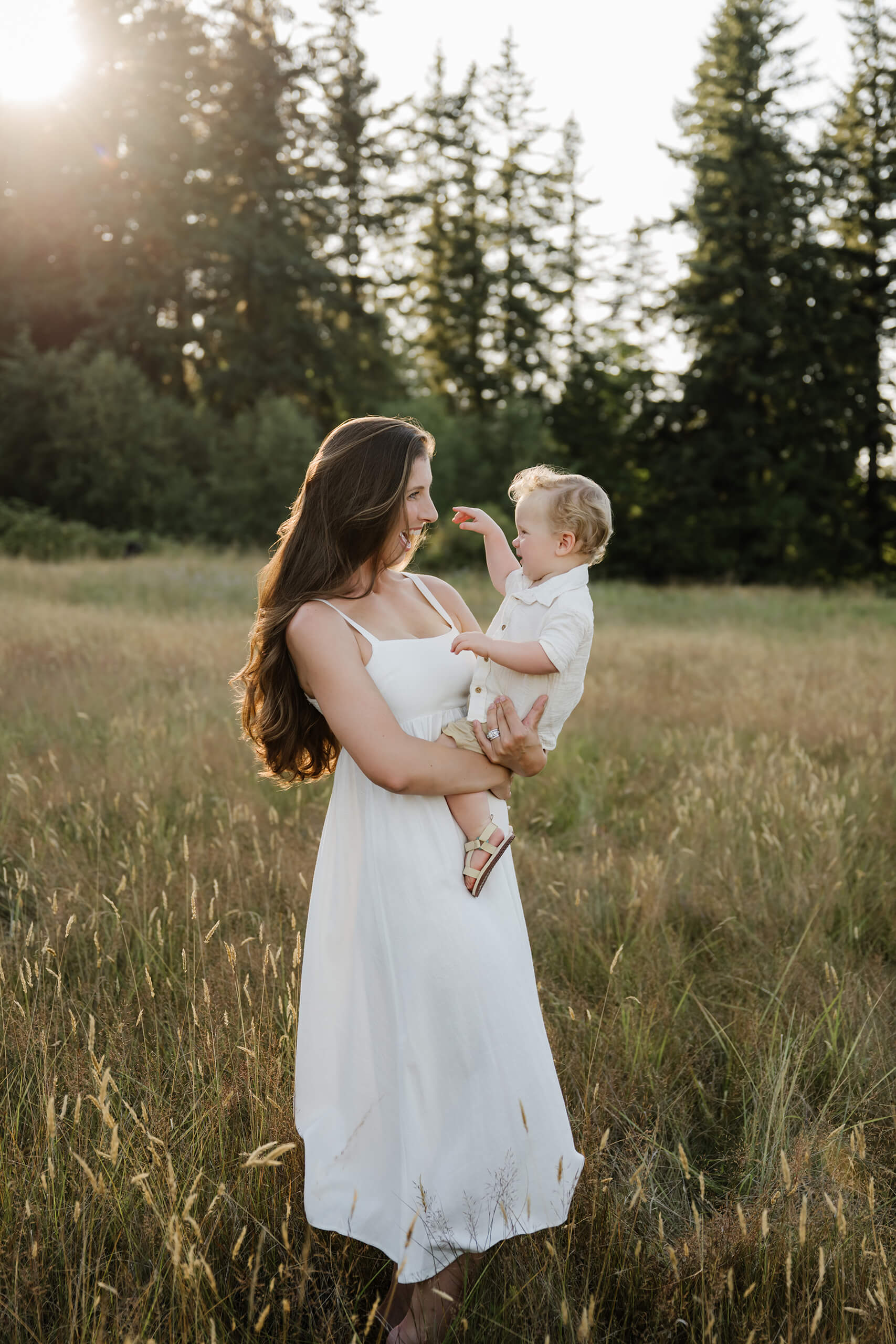 Mother holding her toddler in a grassy field during a sunlit outdoor family session.