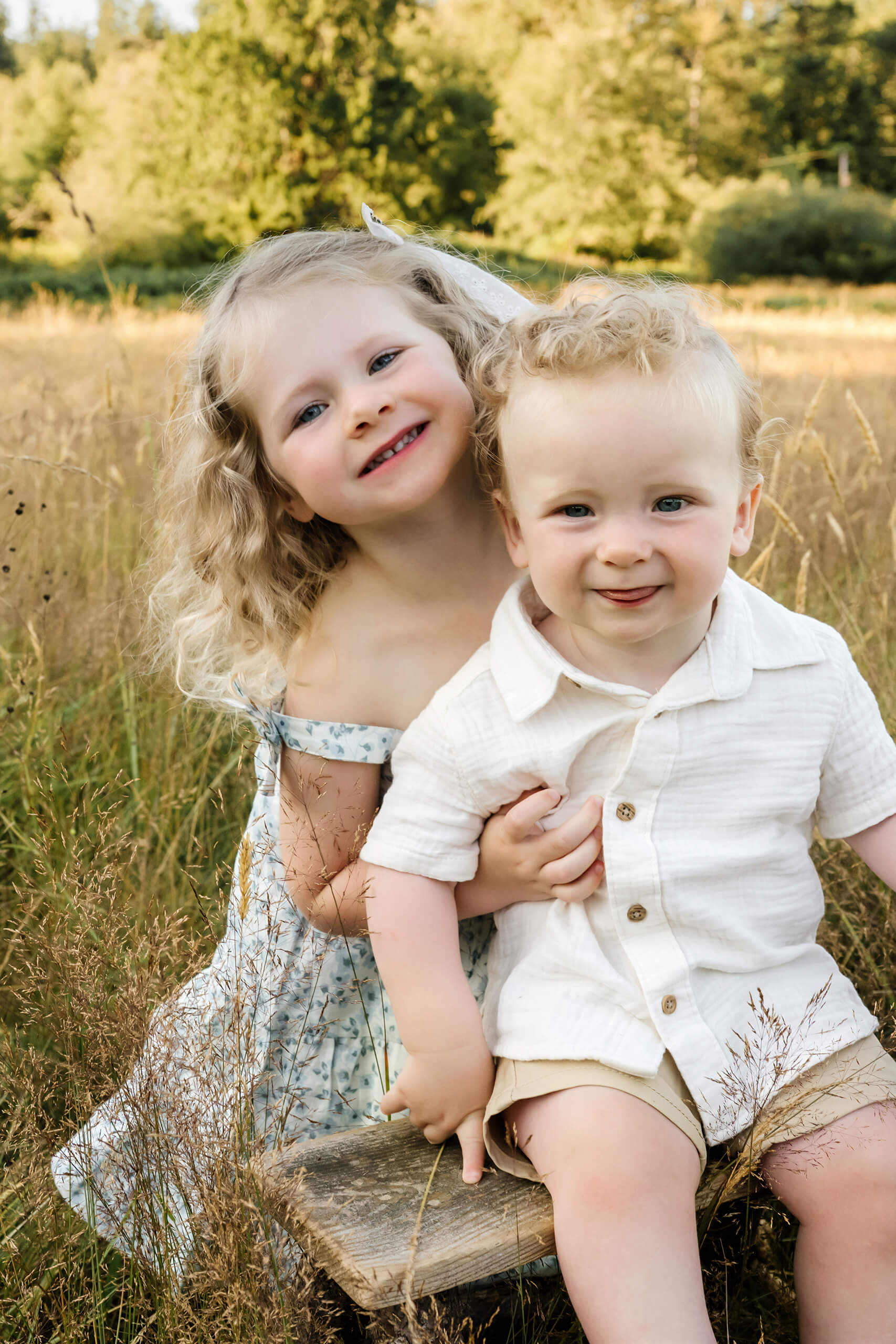 Young brother and sister sitting together in tall grass during a family photo session.