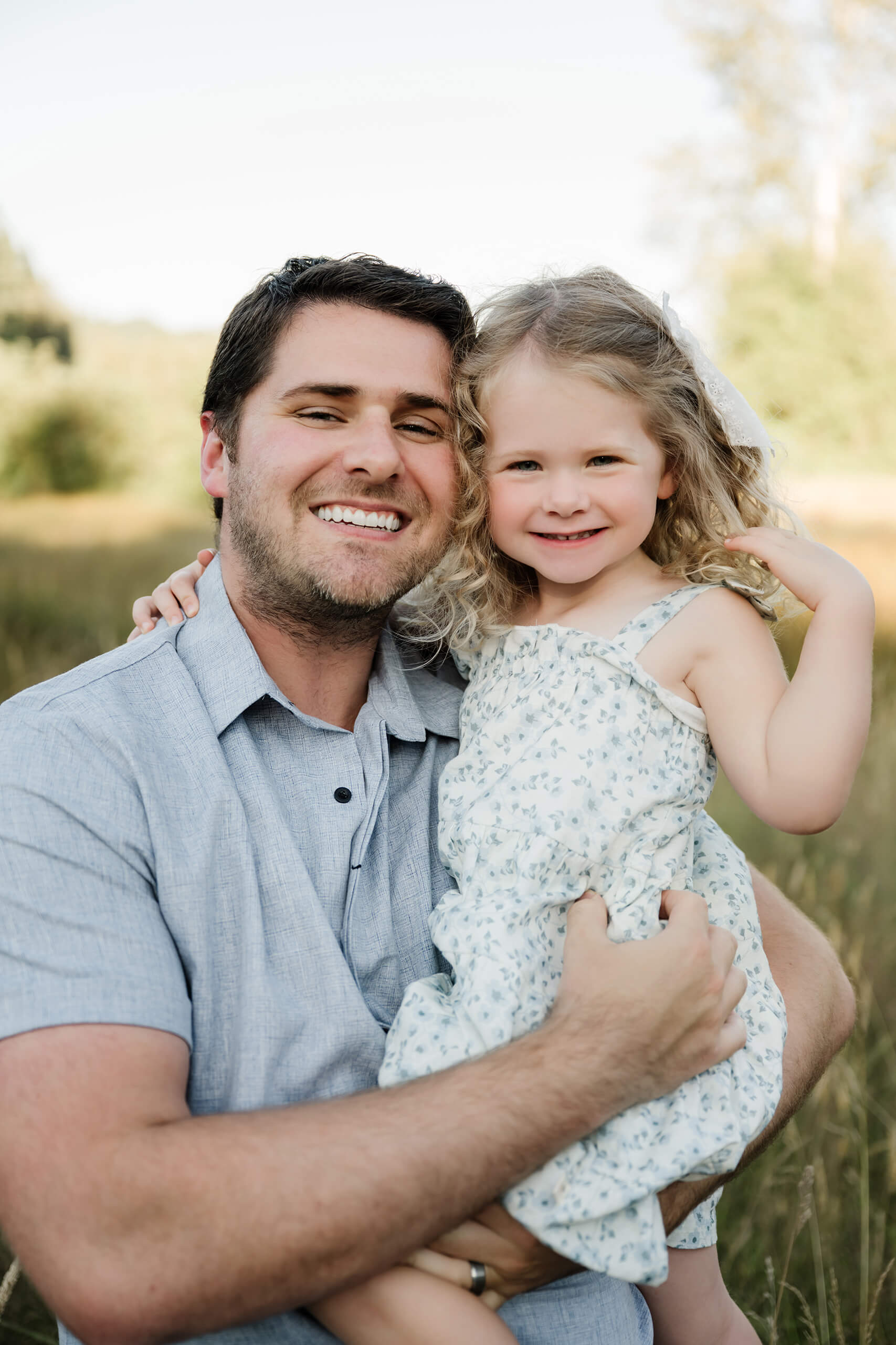 Father holding his daughter for a close-up portrait in a golden outdoor field.