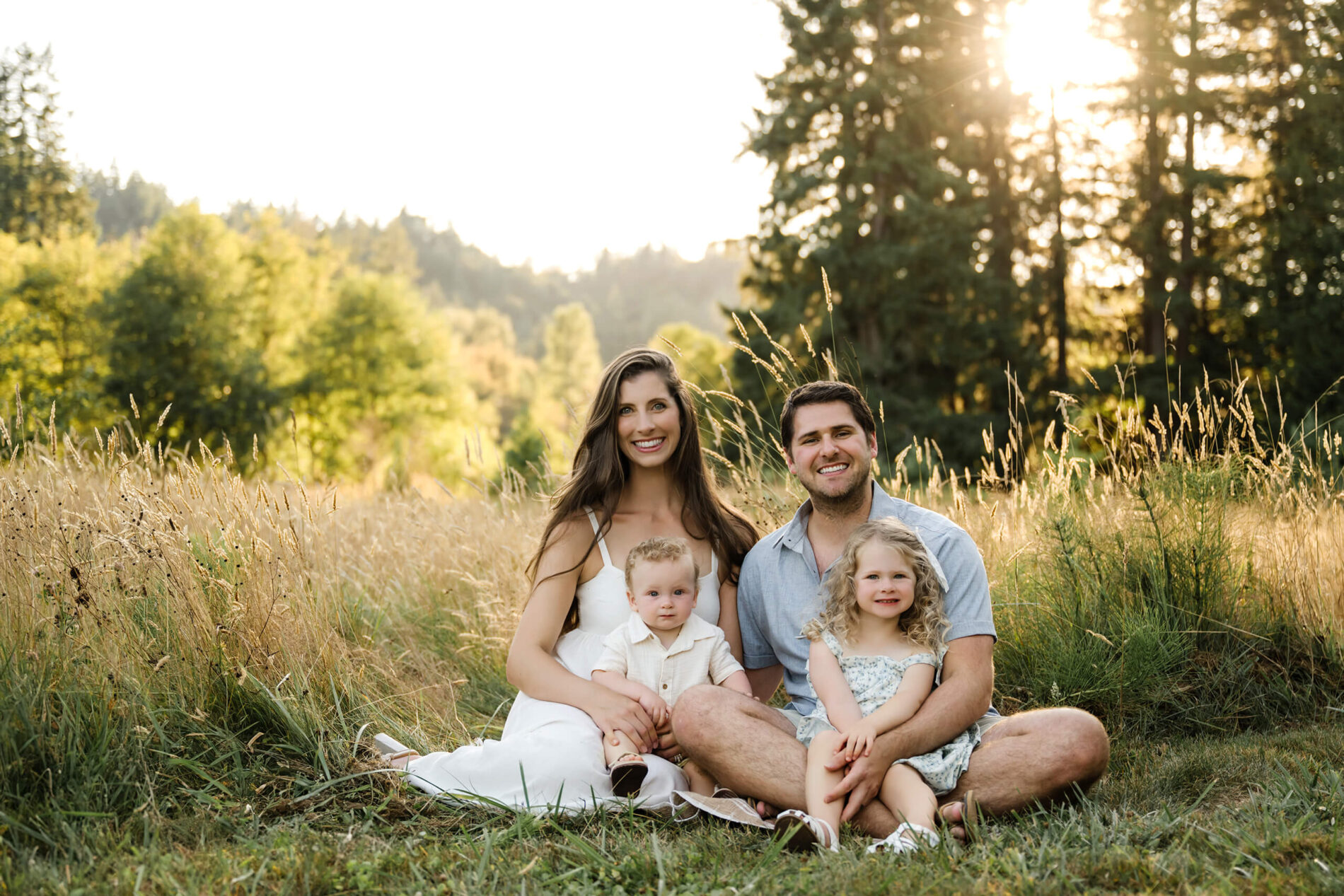 Family of four sitting together in a grassy field with warm evening light behind them.