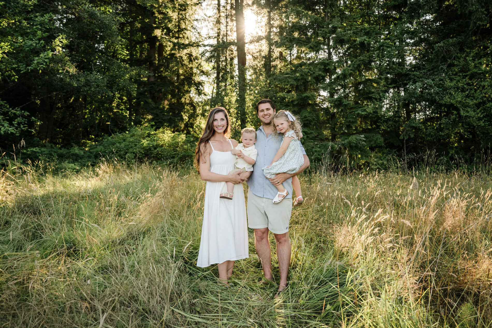 Parents holding their two young children in tall grass during an outdoor family session near the trees.