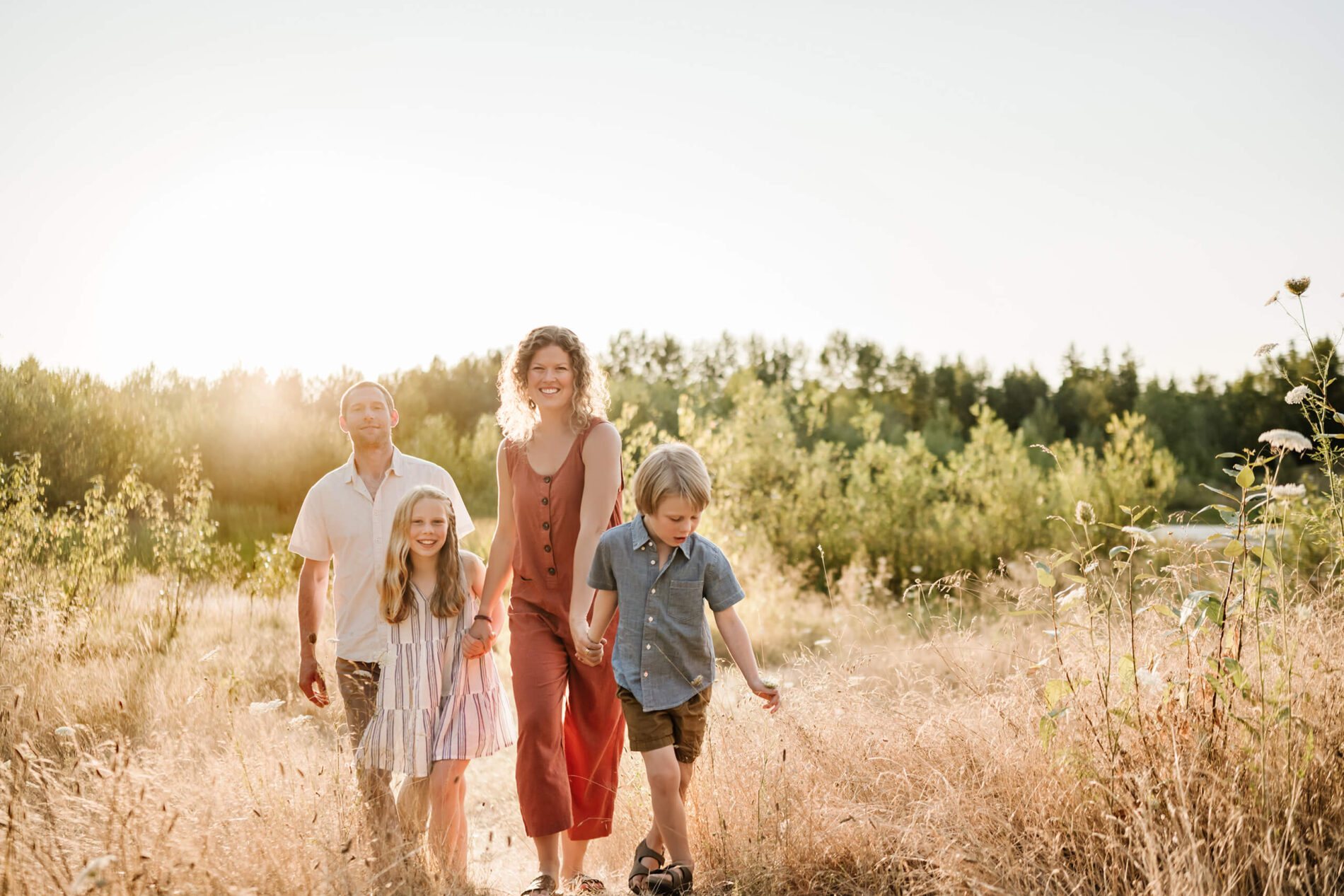 Parents and two children walking along a sunny path through tall summer grass.
