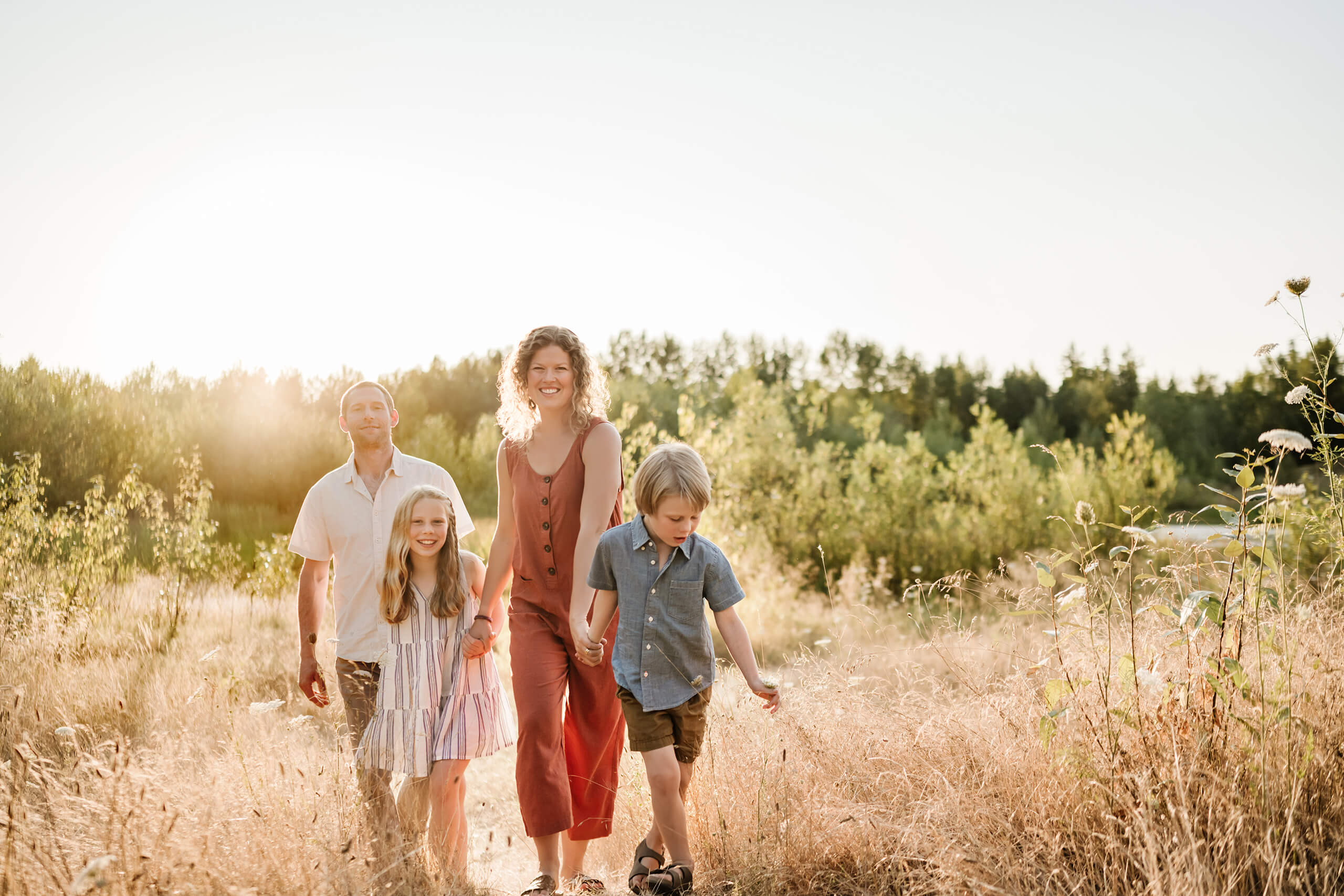 Parents and two children walking along a sunny path through tall summer grass.
