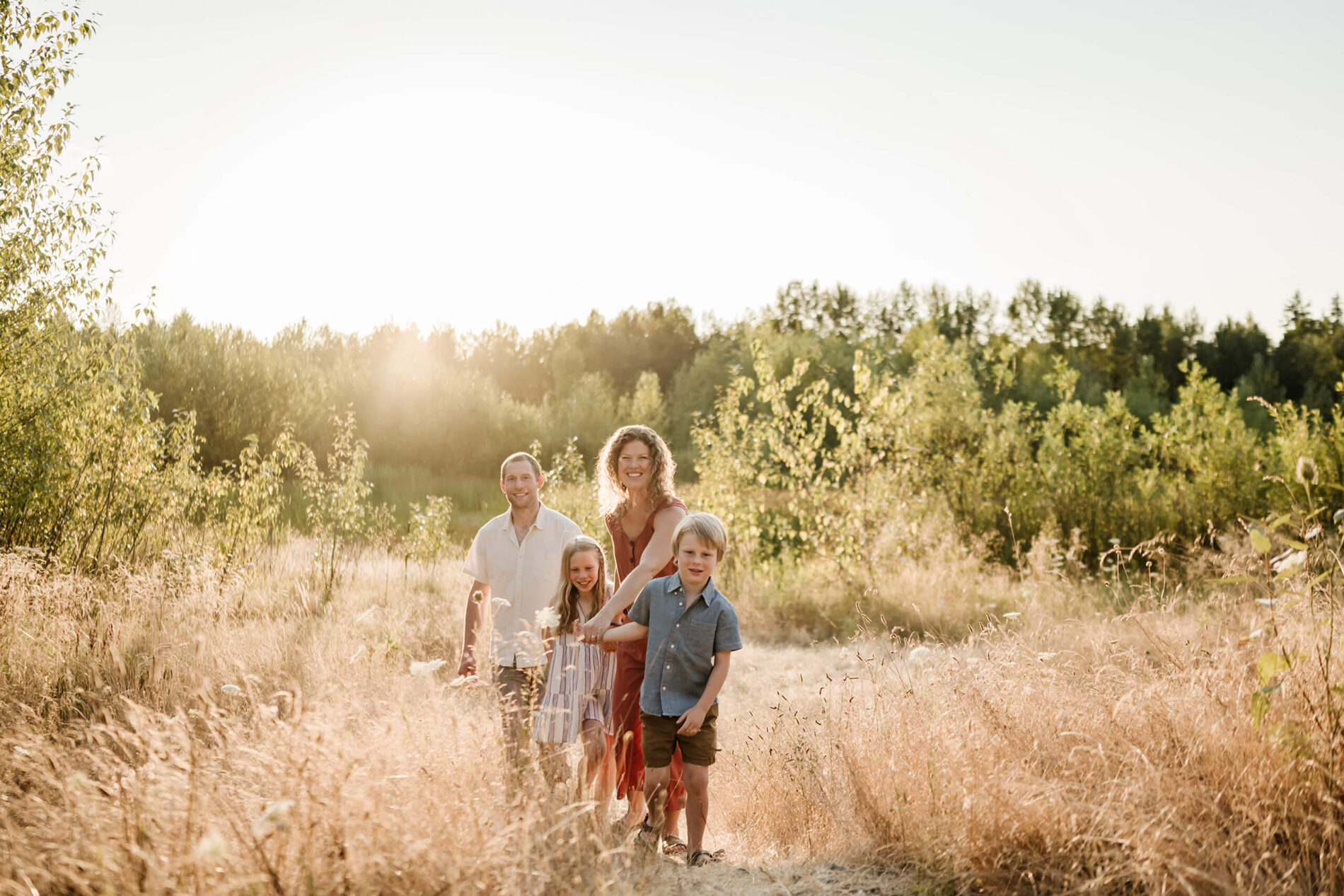 Family walking through tall golden grass beside a pond during an outdoor family photo session.