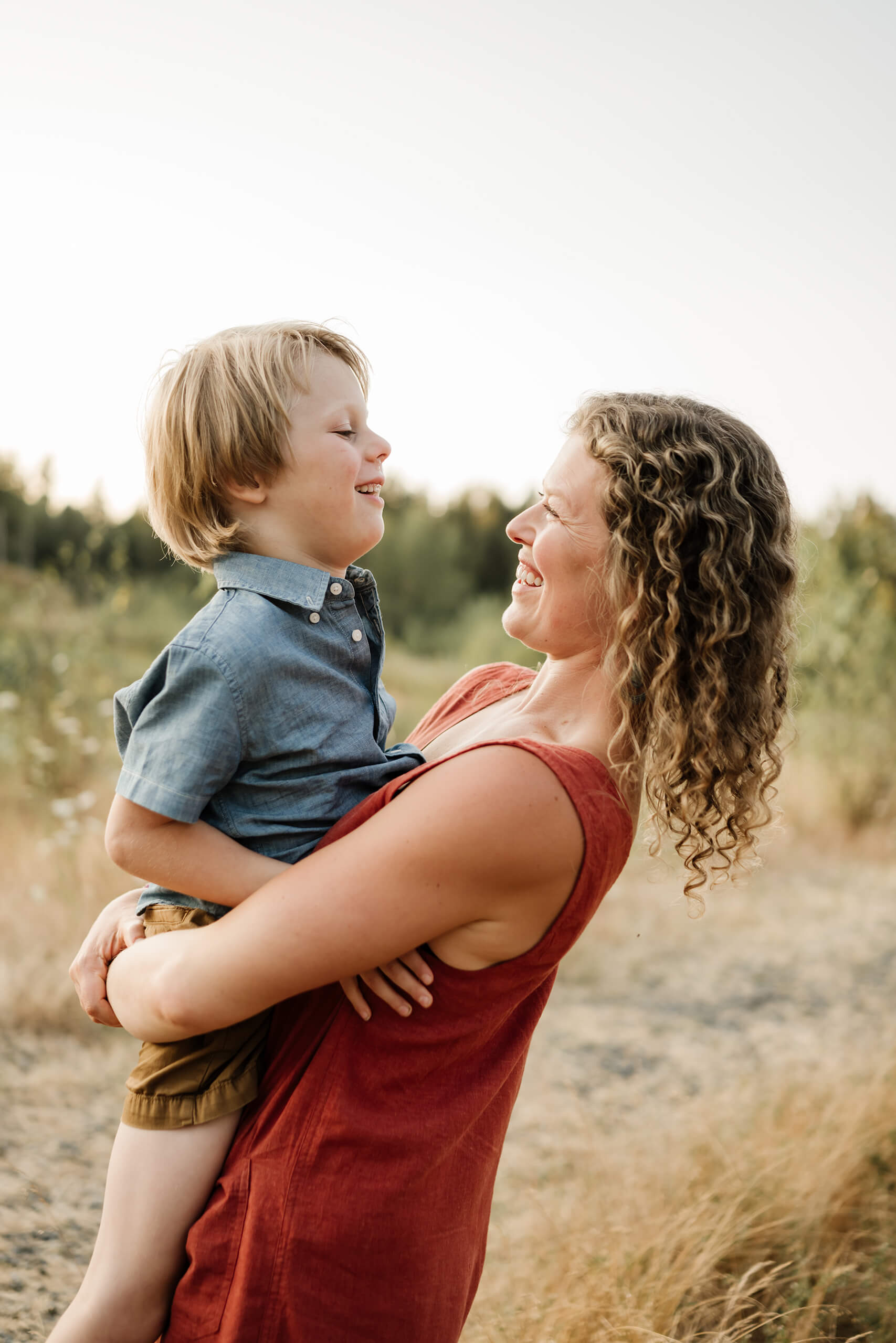 Mother holding her son and smiling at him in a warm outdoor field.