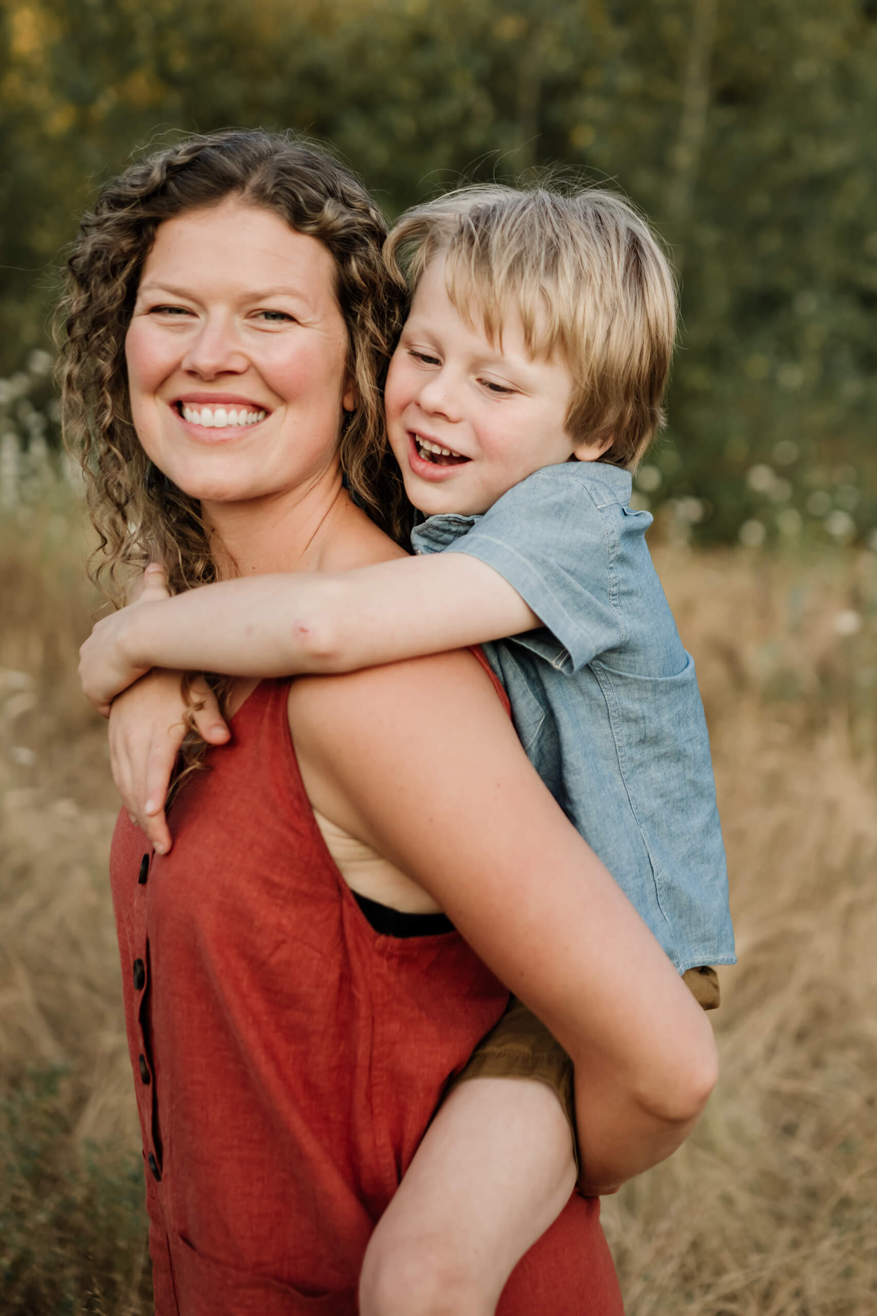 Mother carrying her son on her back in tall dry grass during a family session.