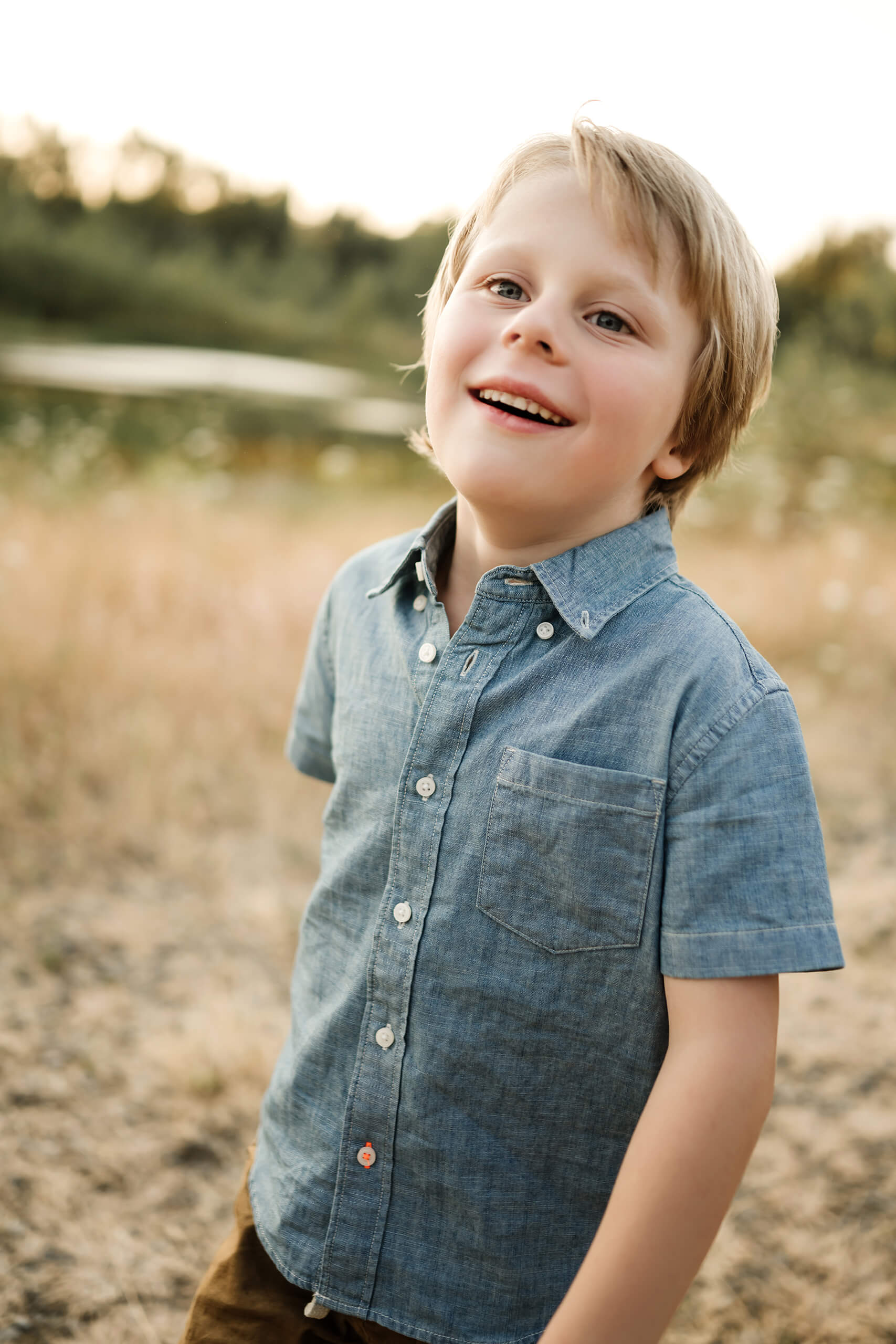 Young boy smiling in a golden field near the water during an outdoor family photo session.