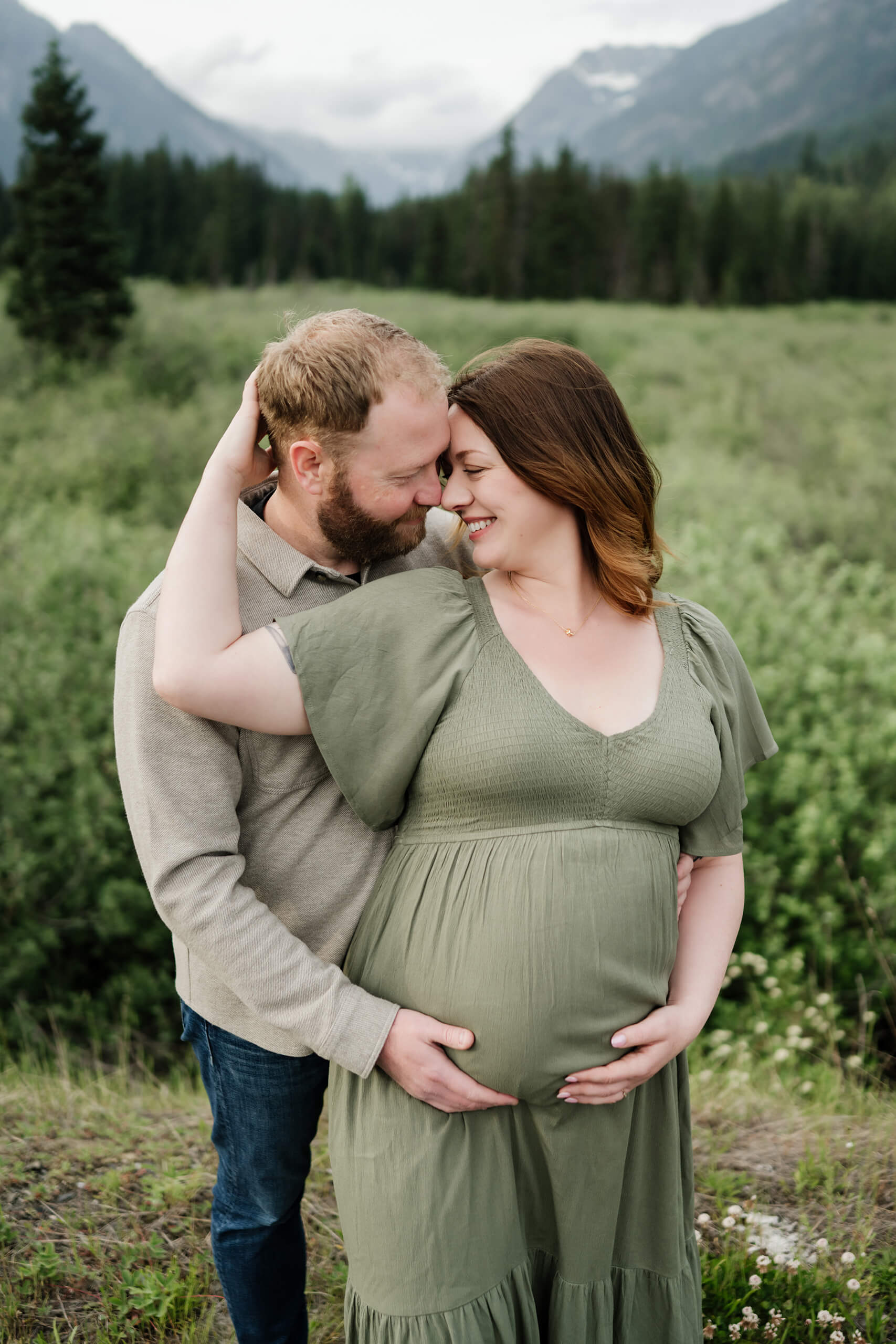 Expecting couple embracing in a green mountain field during an outdoor maternity session.