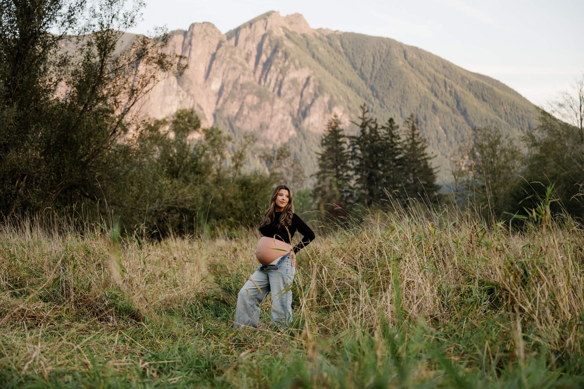 Pregnant woman standing in a grassy mountain field for an outdoor maternity portrait.