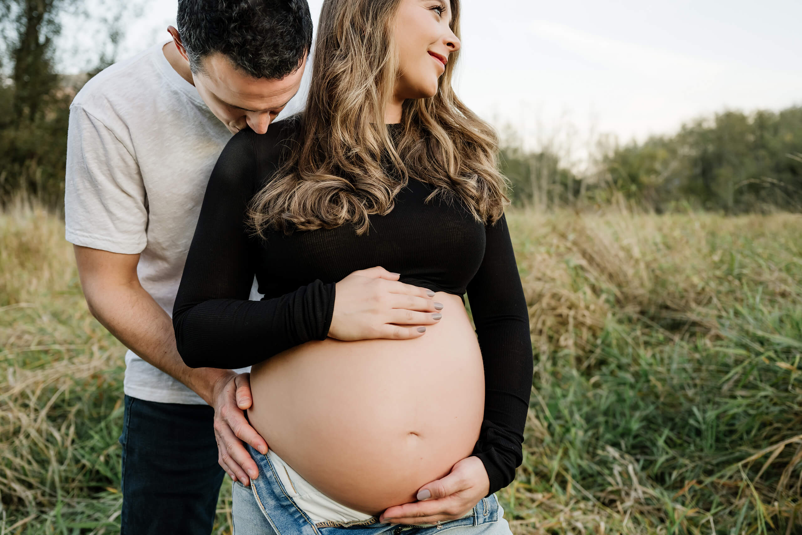Expecting couple holding the baby bump in a grassy field during an outdoor maternity session.