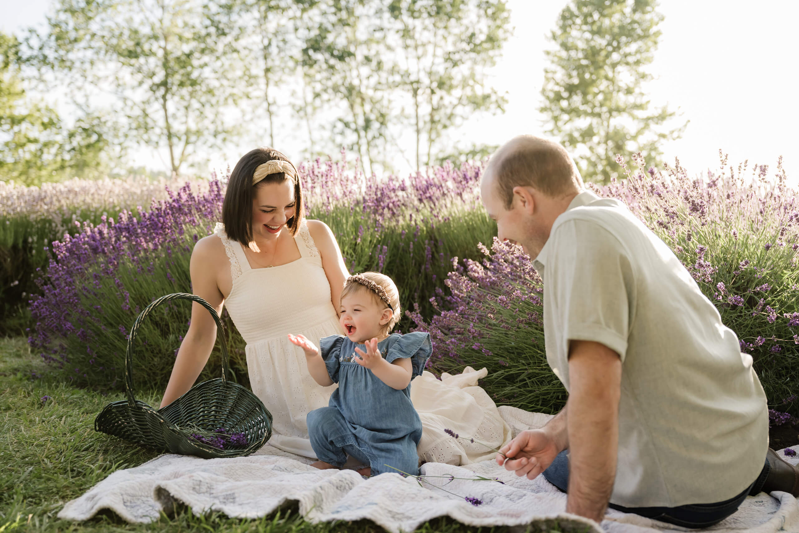Parents sitting with their toddler daughter on a blanket in a lavender field during an outdoor family session.