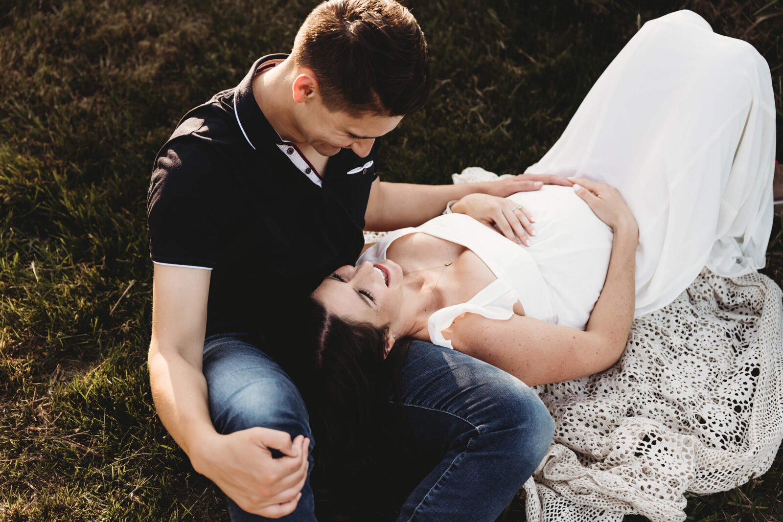 Expecting parents laughing together on a blanket during a relaxed outdoor maternity session.