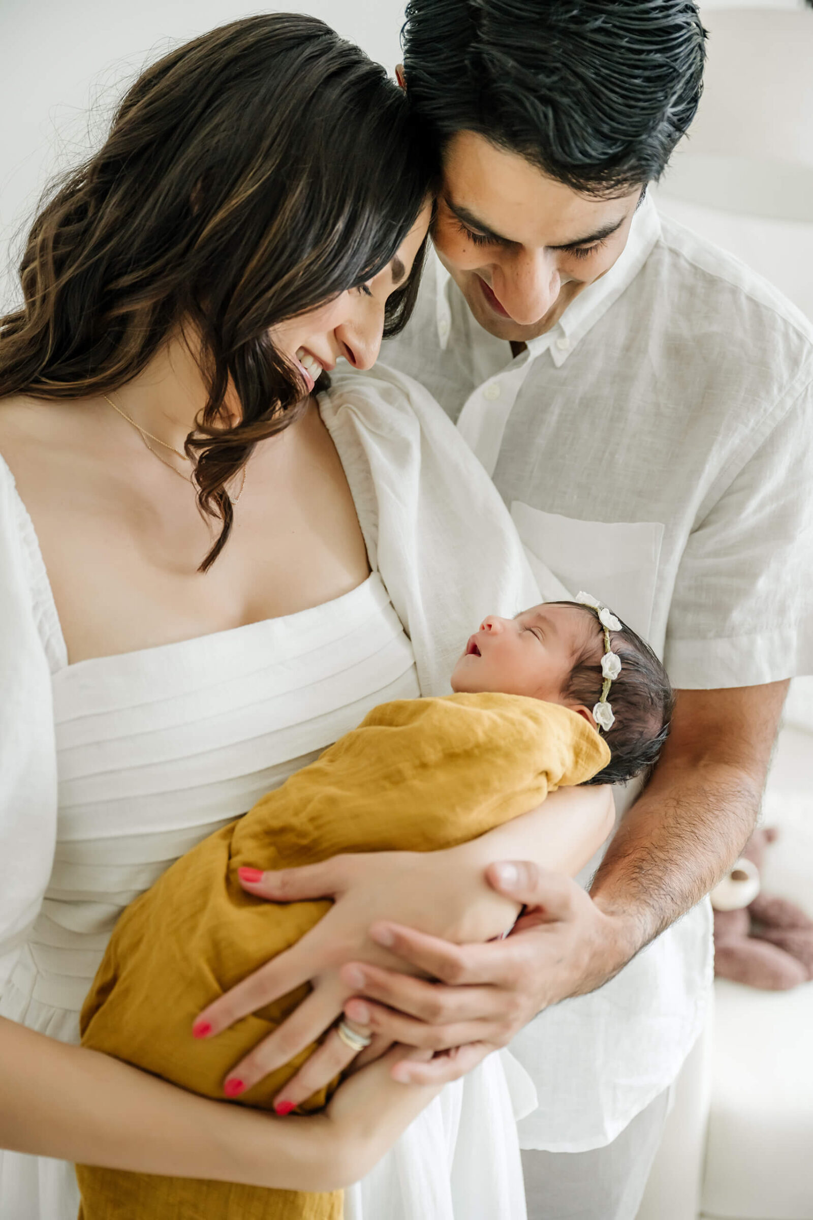 New parents smiling at their newborn baby during a soft in-home newborn session, part of a maternity and newborn photography package.