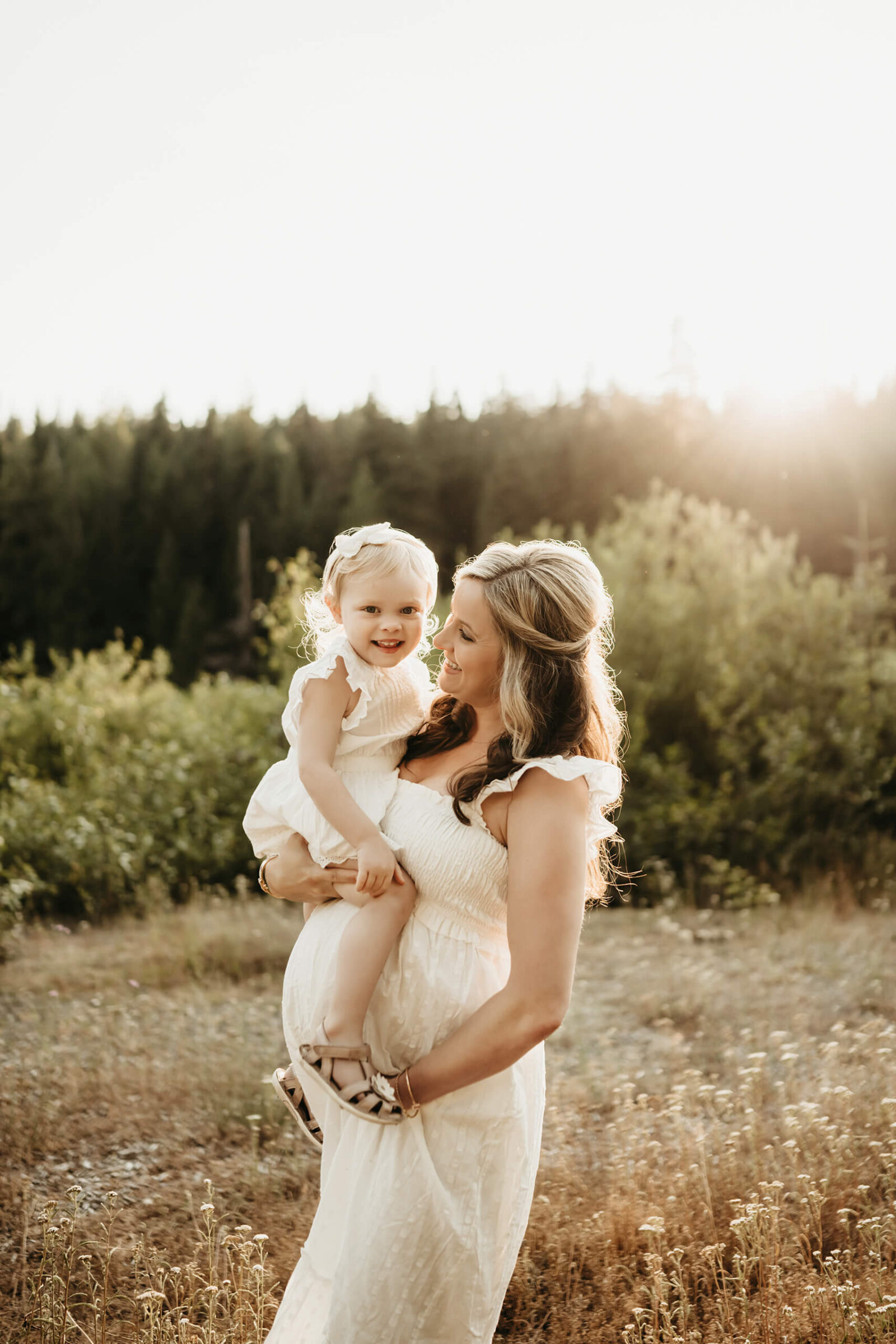 Expecting mom holding her young daughter in warm golden light during a natural outdoor maternity session near Seattle.
