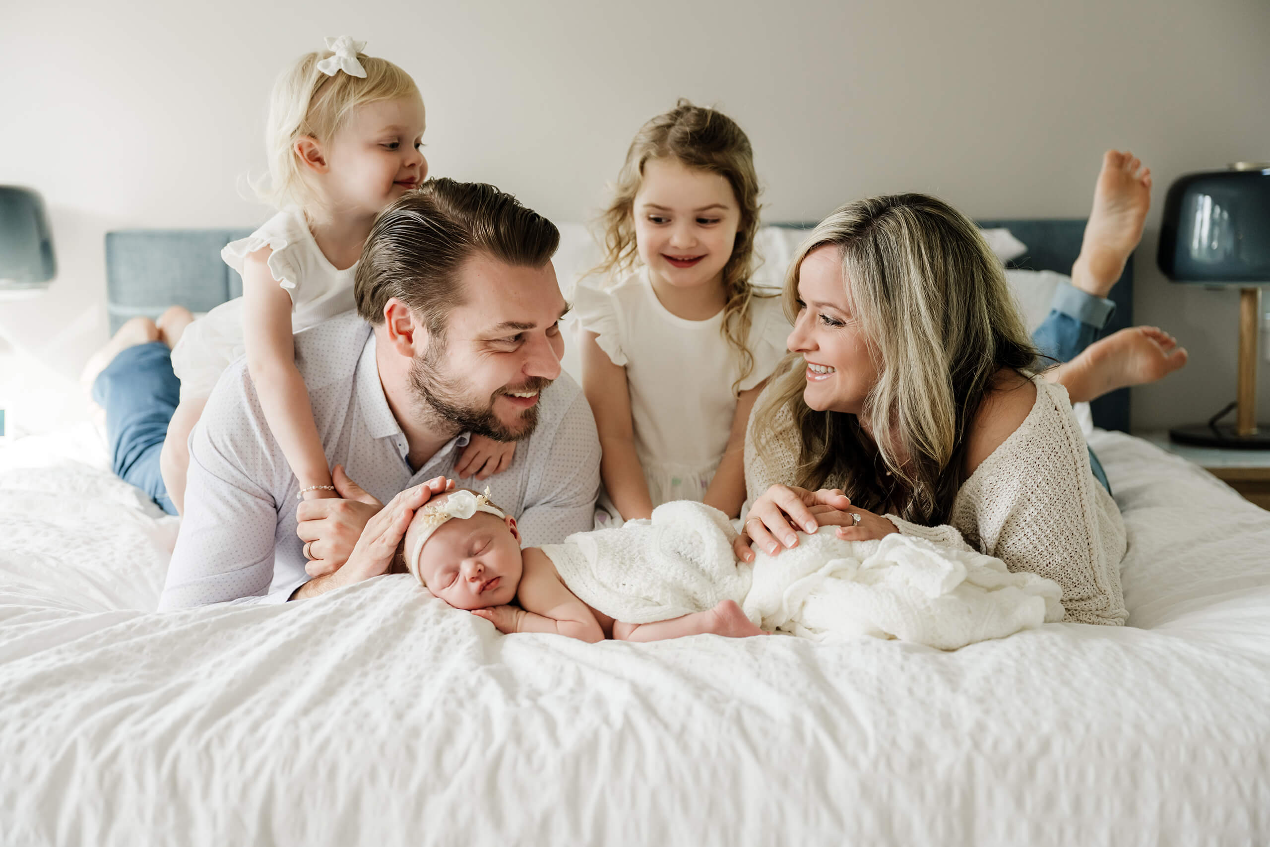 Family cuddling together on the bed with their newborn baby during a natural in-home newborn session.