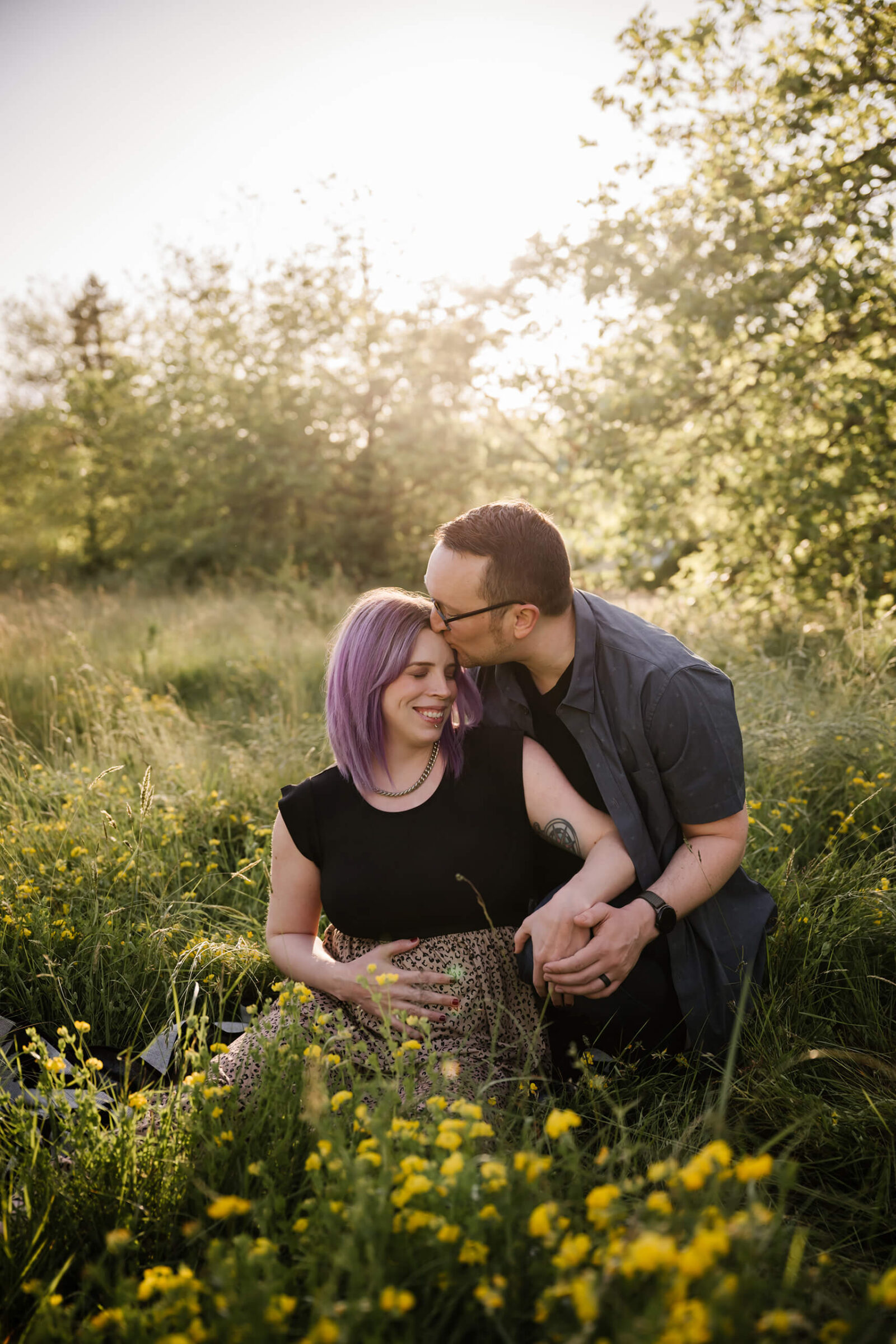 Expecting parents cuddling in a sunlit field during a warm outdoor maternity session at Seattle Discovery Park.