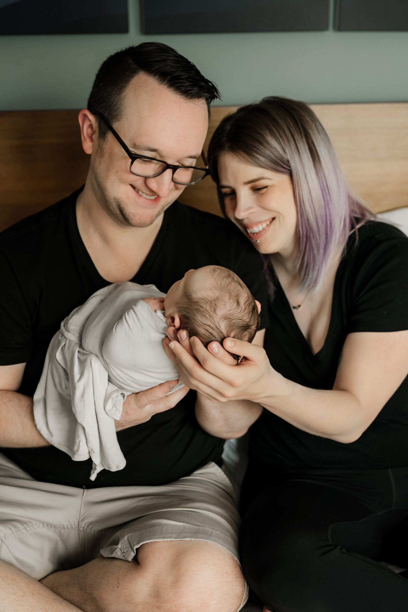 Parents smiling at their newborn baby during a natural in-home newborn session, part of a maternity and newborn photography package.