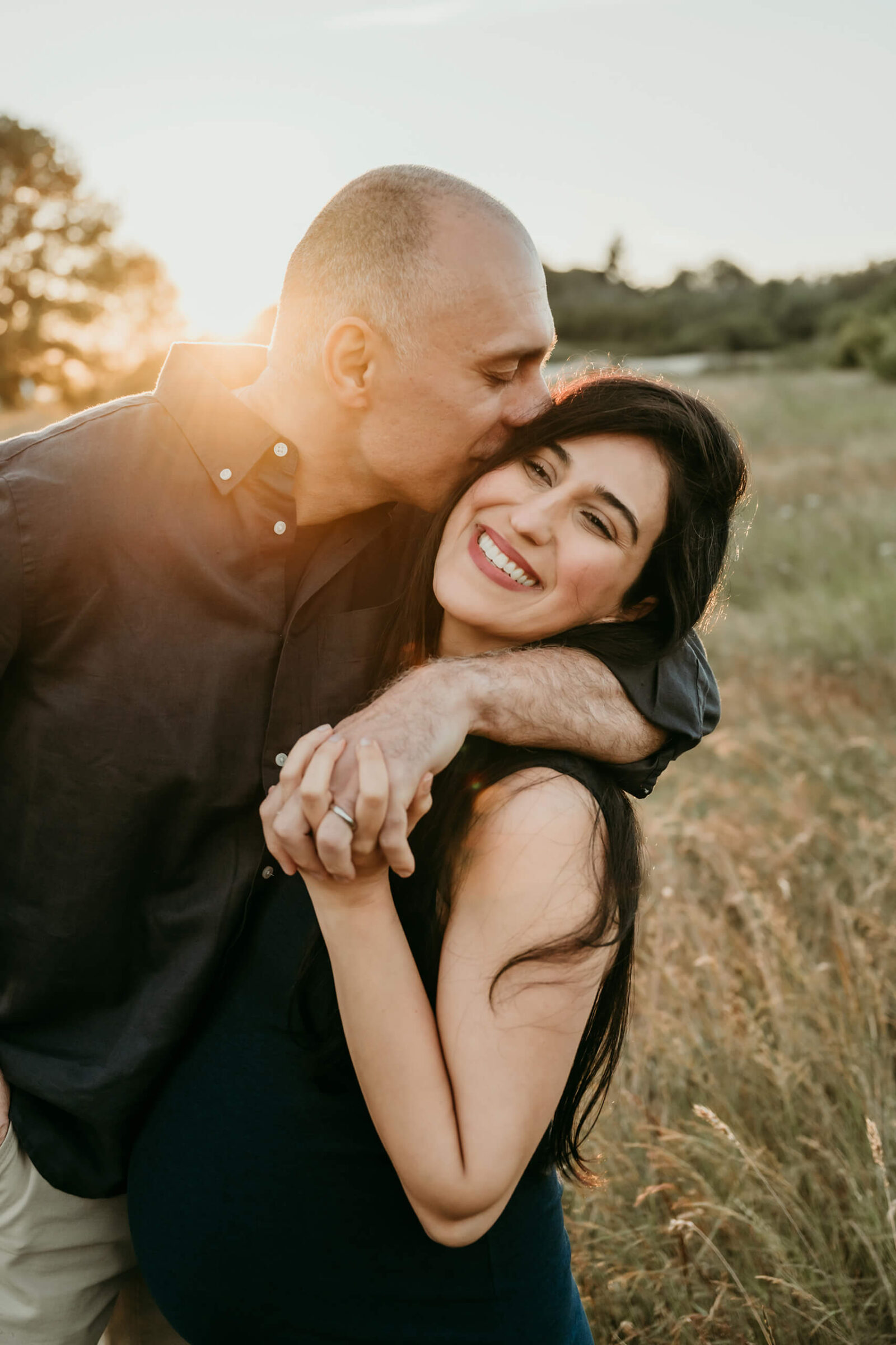 Expecting parents cuddling in a golden field during a warm outdoor maternity session.