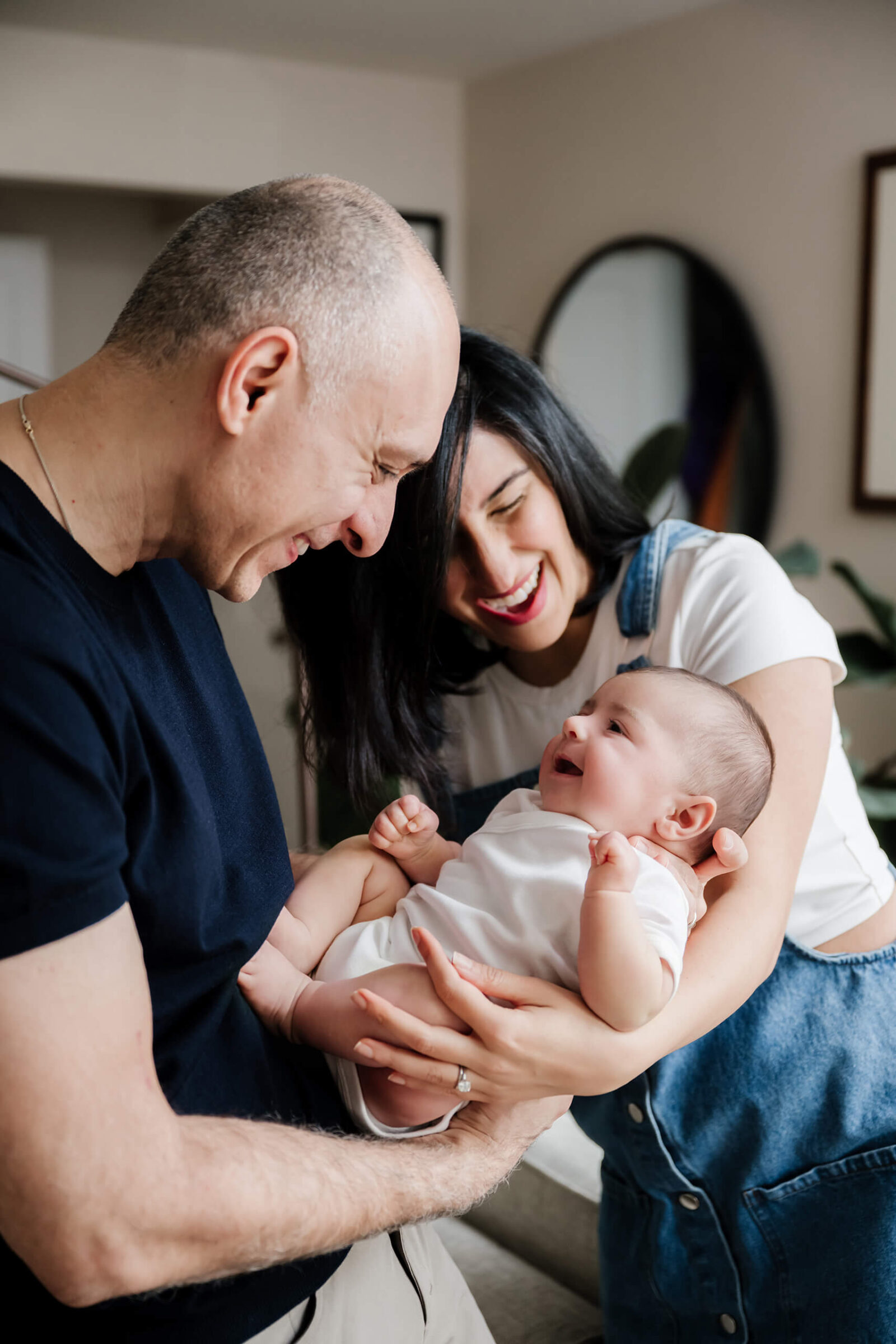 Parents smiling and cuddling their baby at home during a natural in-home newborn lifestyle session.